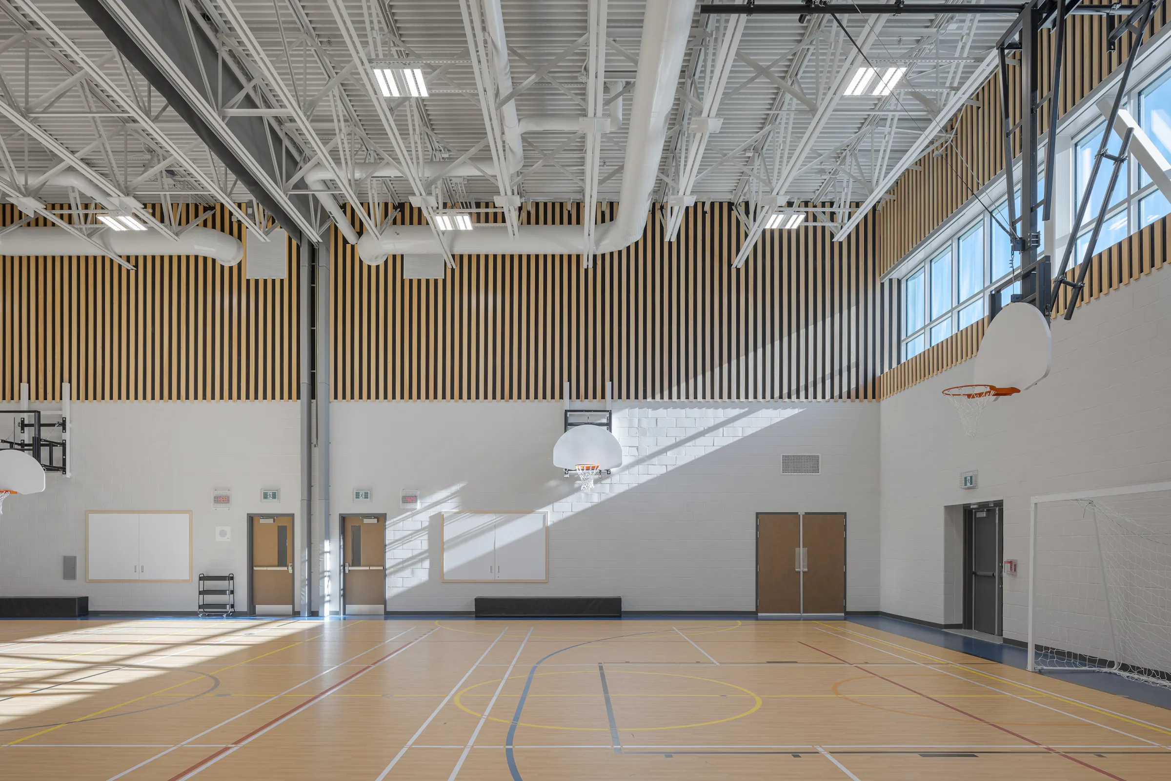 Gymnase de l'École des Saules, L'Assomption. Boiseries verticales, structure métallique apparente et éclairage naturel. Photo : Studio Tarmac.