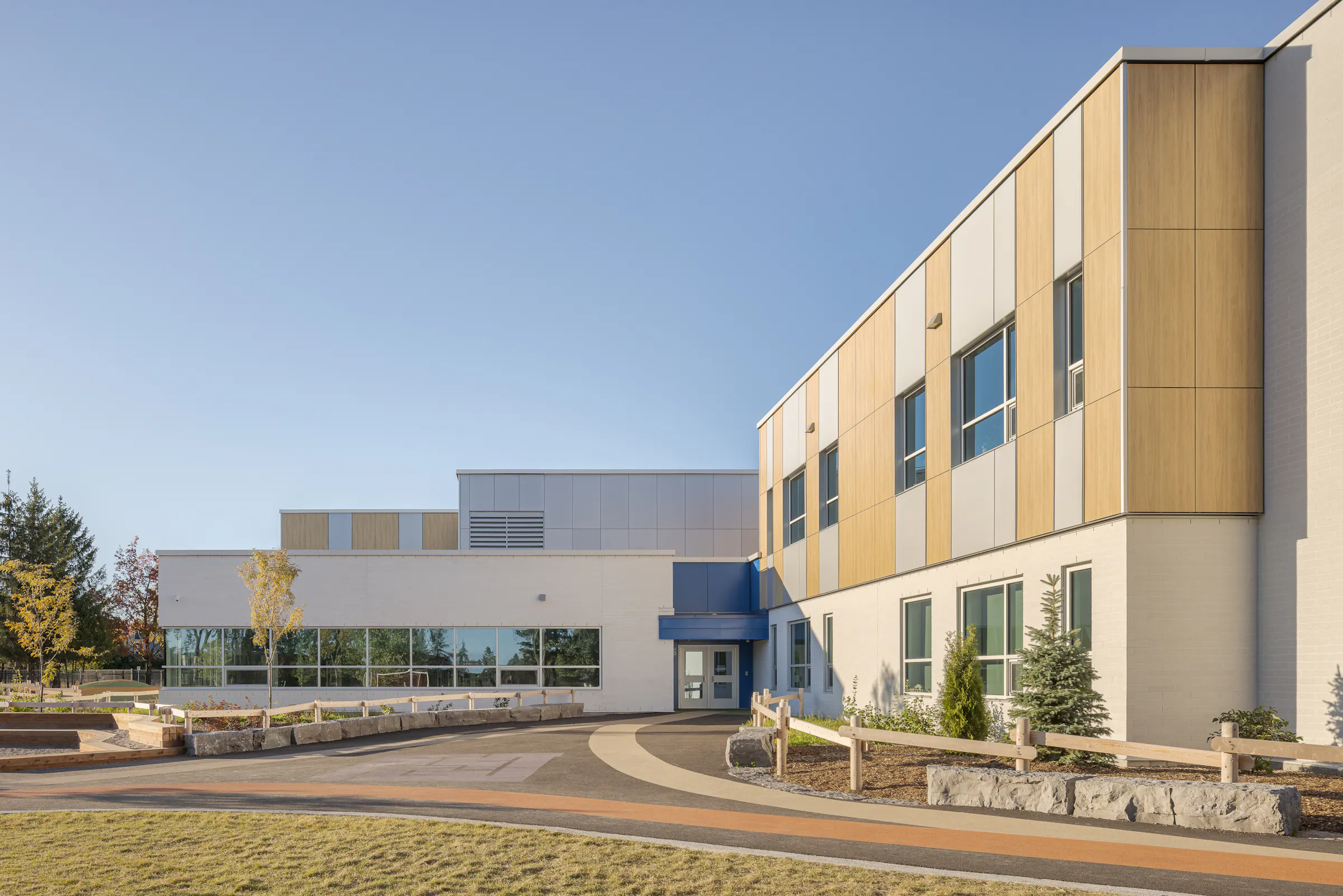 Vue d'ensemble de l'entrée principale de l'École des Saules, L'Assomption. Volumétrie en L et aménagements paysagers. Photo : TARMAC - Damien Ligiardi.