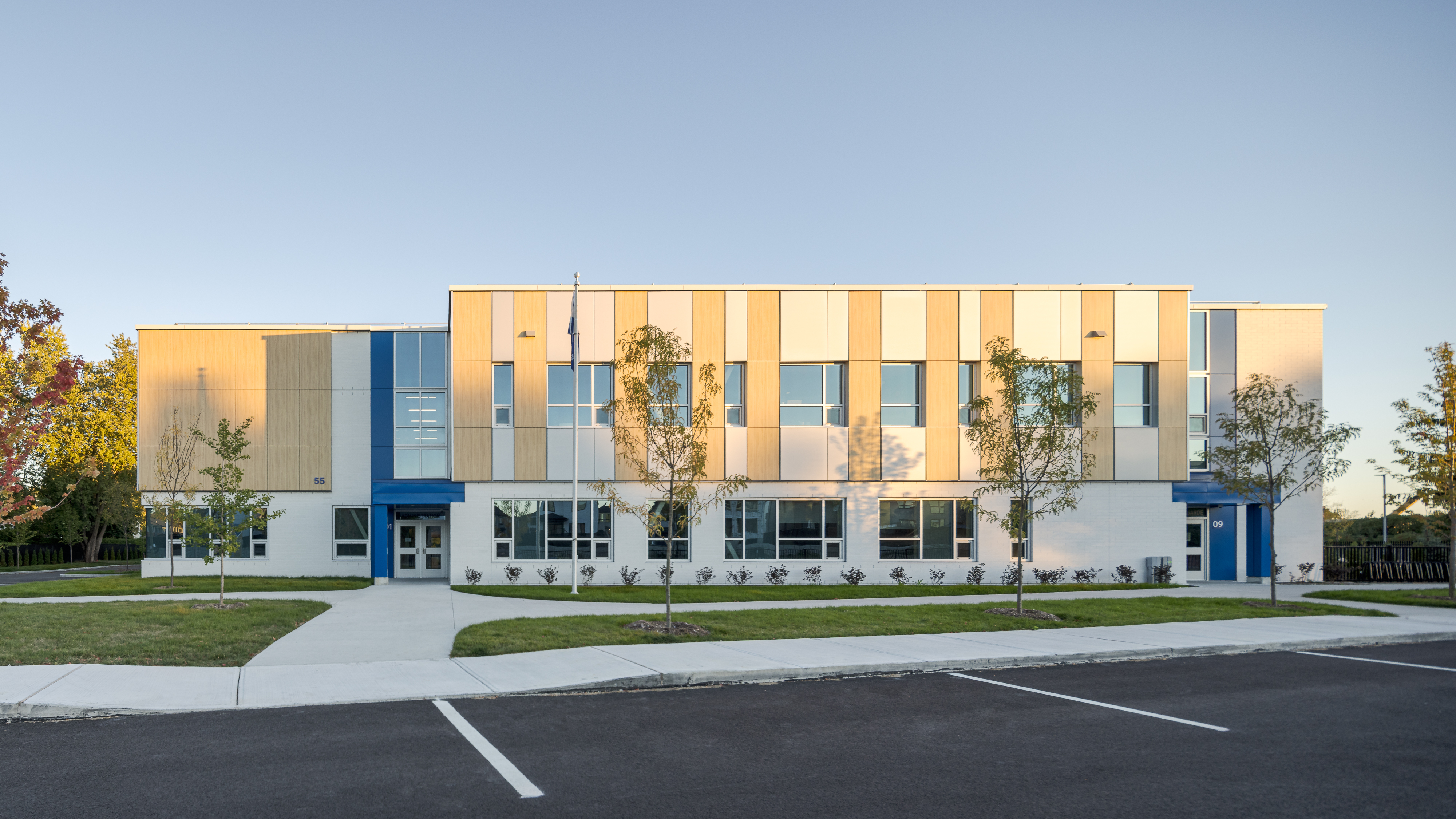 Vue frontale de l'École des Saules, L'Assomption en lumière dorée. Façade bois, blanc et bleu sur fond de ciel dégagé. Photo : TARMAC - Damien Ligiardi.
