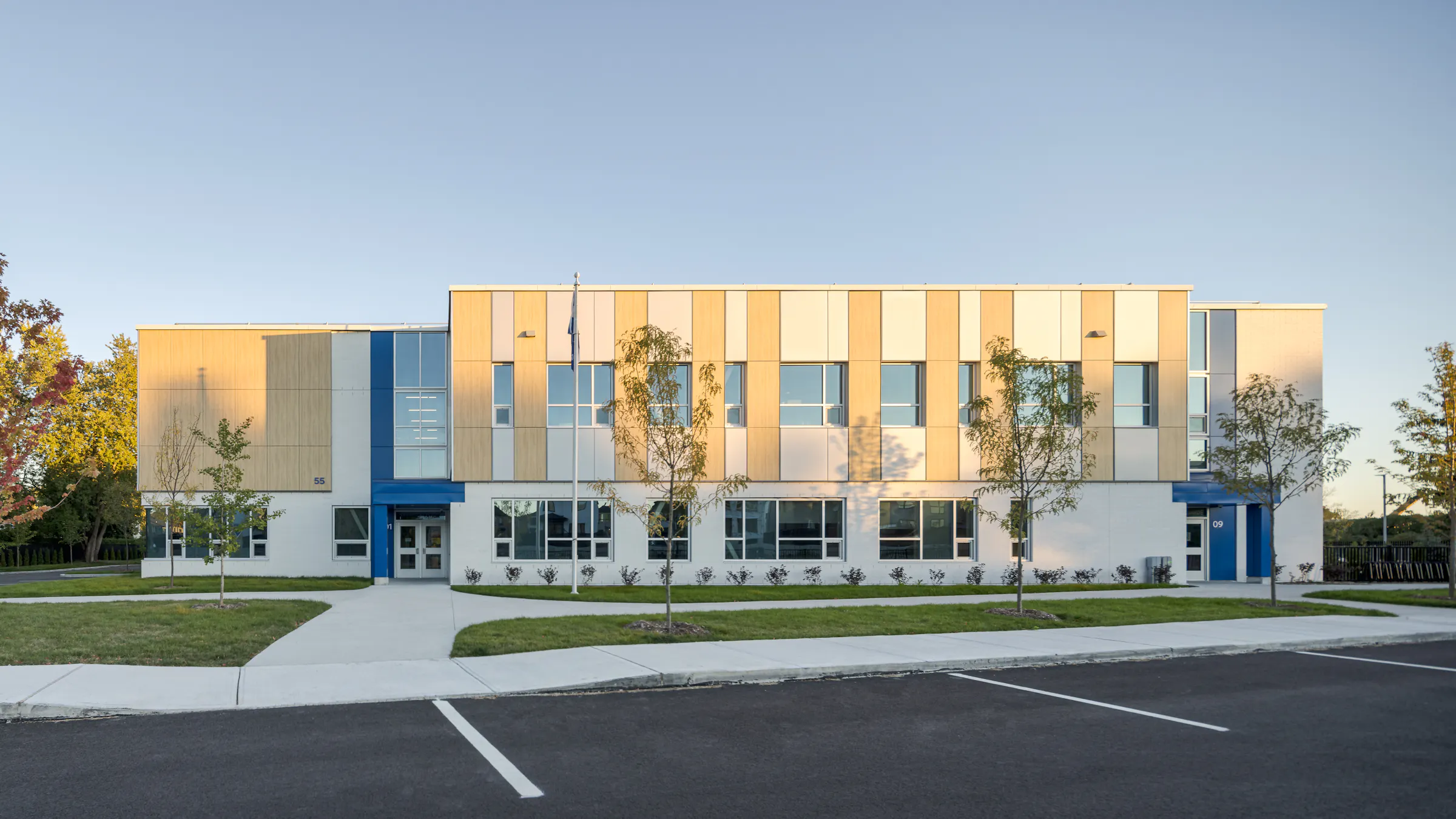 Vue frontale de l'École des Saules, L'Assomption en lumière dorée. Façade bois, blanc et bleu sur fond de ciel dégagé. Photo : TARMAC - Damien Ligiardi.