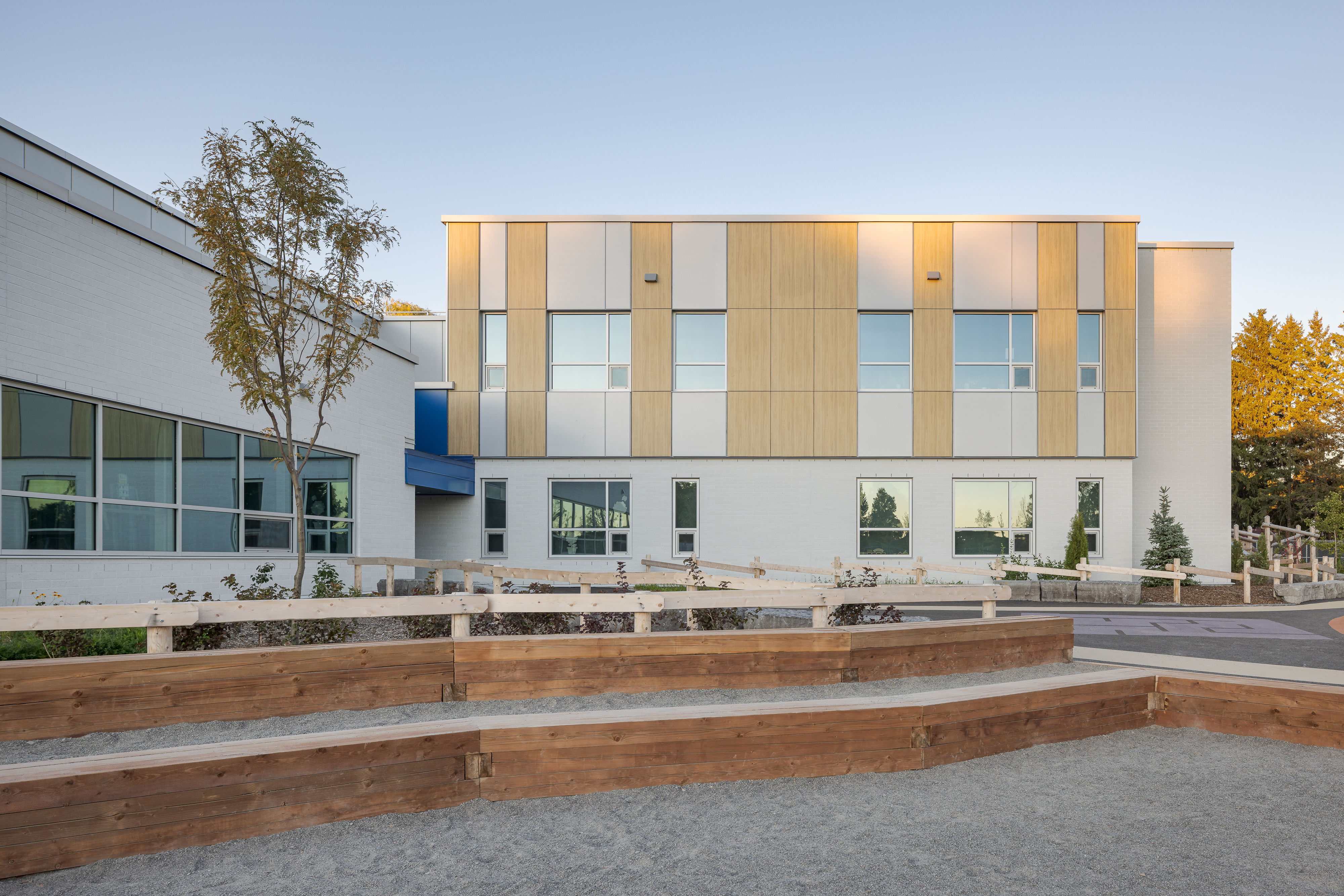 Cour avant de l'École des Saules, L'Assomption avec mobilier extérieur en bois et jeunes arbres. Photo : TARMAC - Damien Ligiardi.