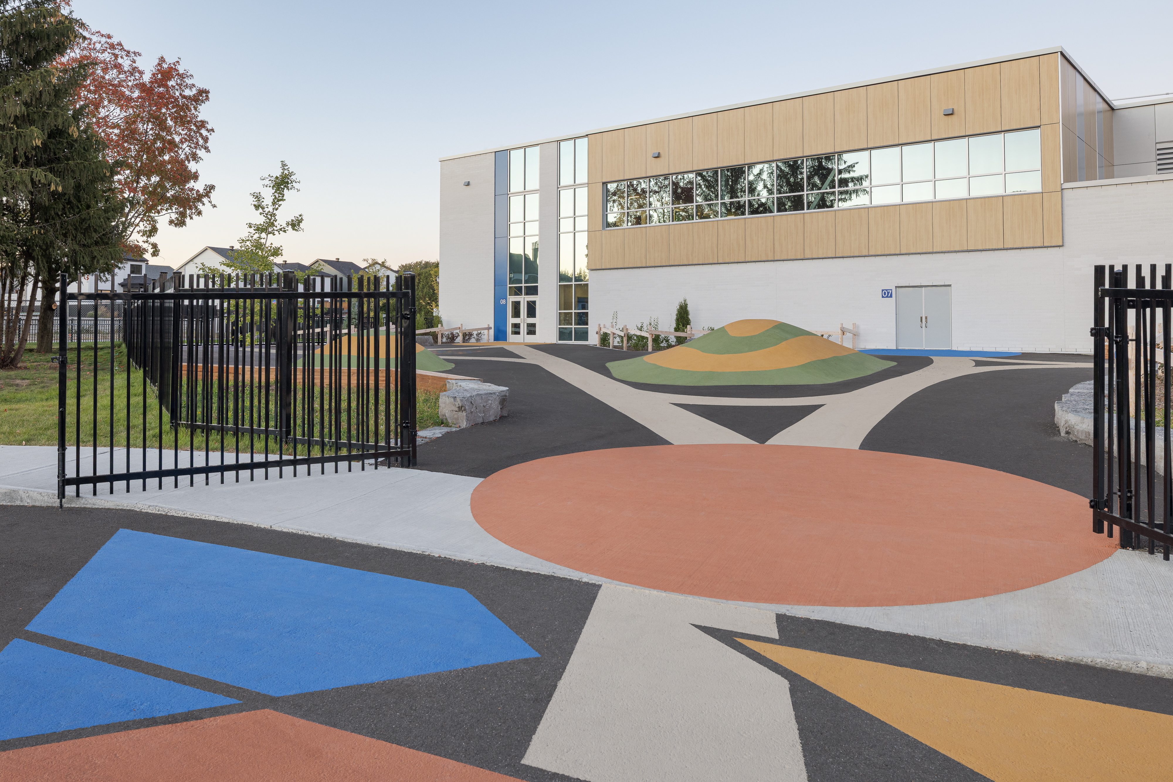 Cour de récréation colorée de l'École des Saules, L'Assomption. Revêtement graphique et butte de jeu, façade gymnase en arrière-plan. Photo : TARMAC - Damien Ligiardi.