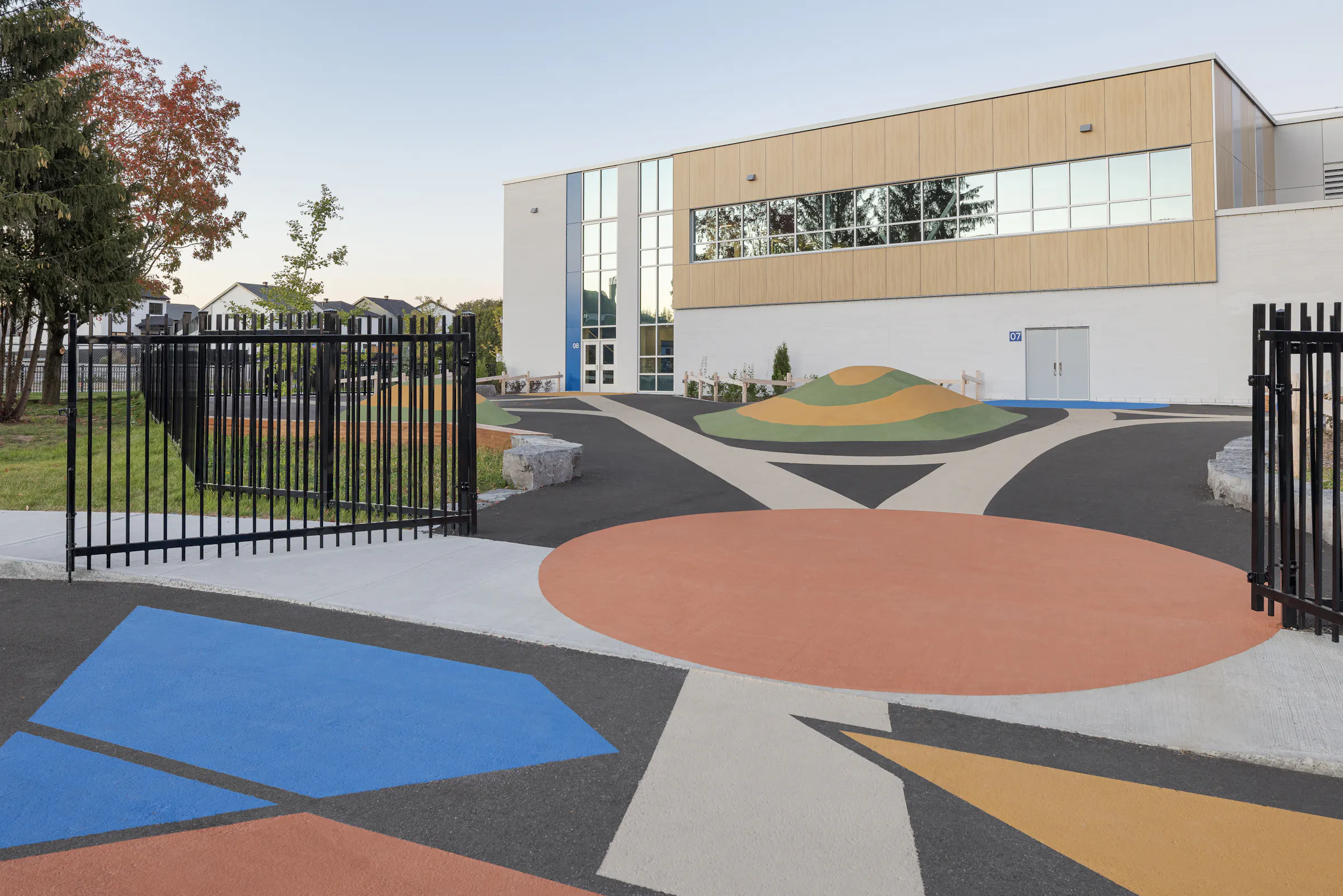 Cour de récréation colorée de l'École des Saules, L'Assomption. Revêtement graphique et butte de jeu, façade gymnase en arrière-plan. Photo : TARMAC - Damien Ligiardi.