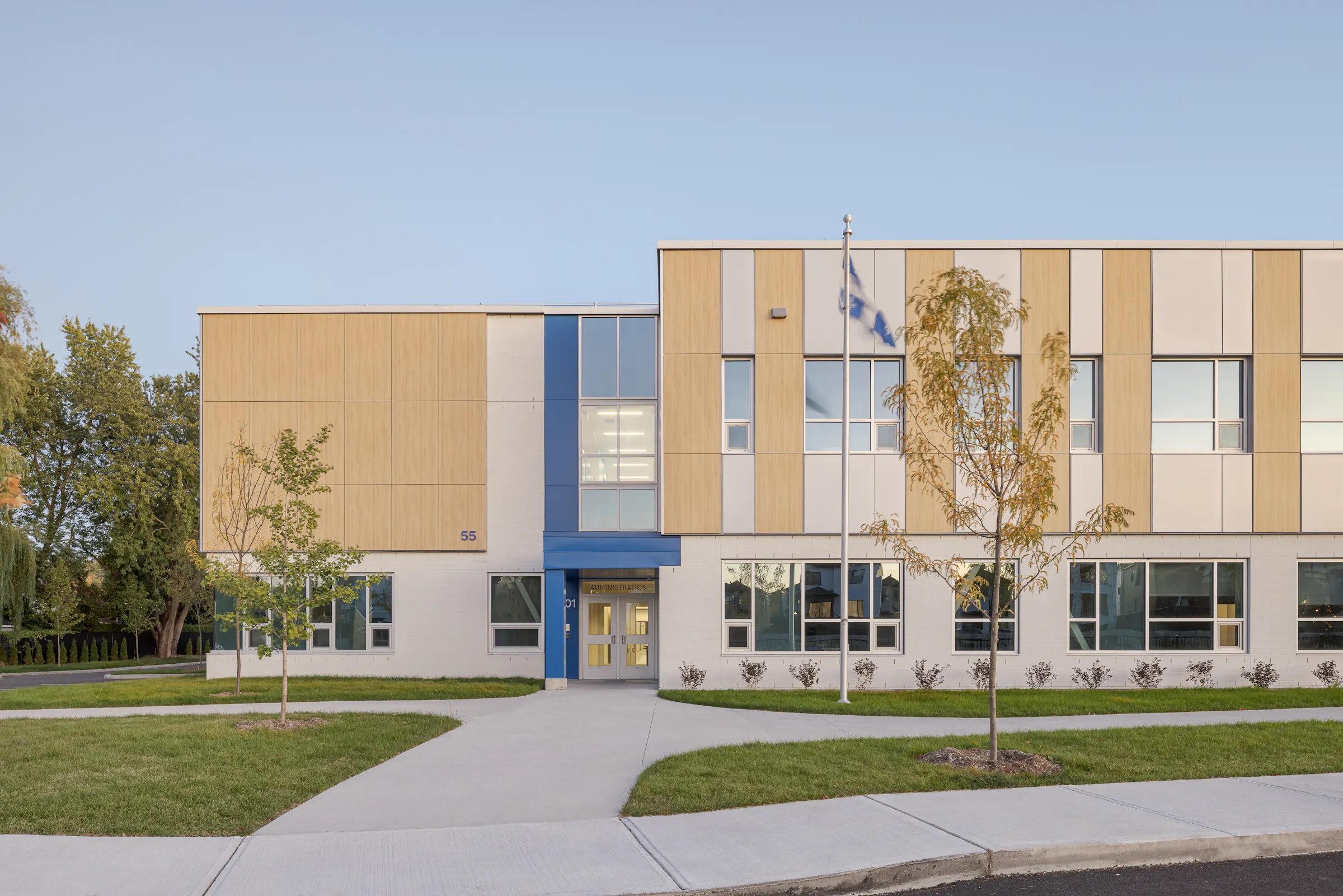 Entrée principale de l'École des Saules, L'Assomption. Façade bois et blanc, accent bleu et mât de drapeau québécois. Photo : TARMAC - Damien Ligiardi.