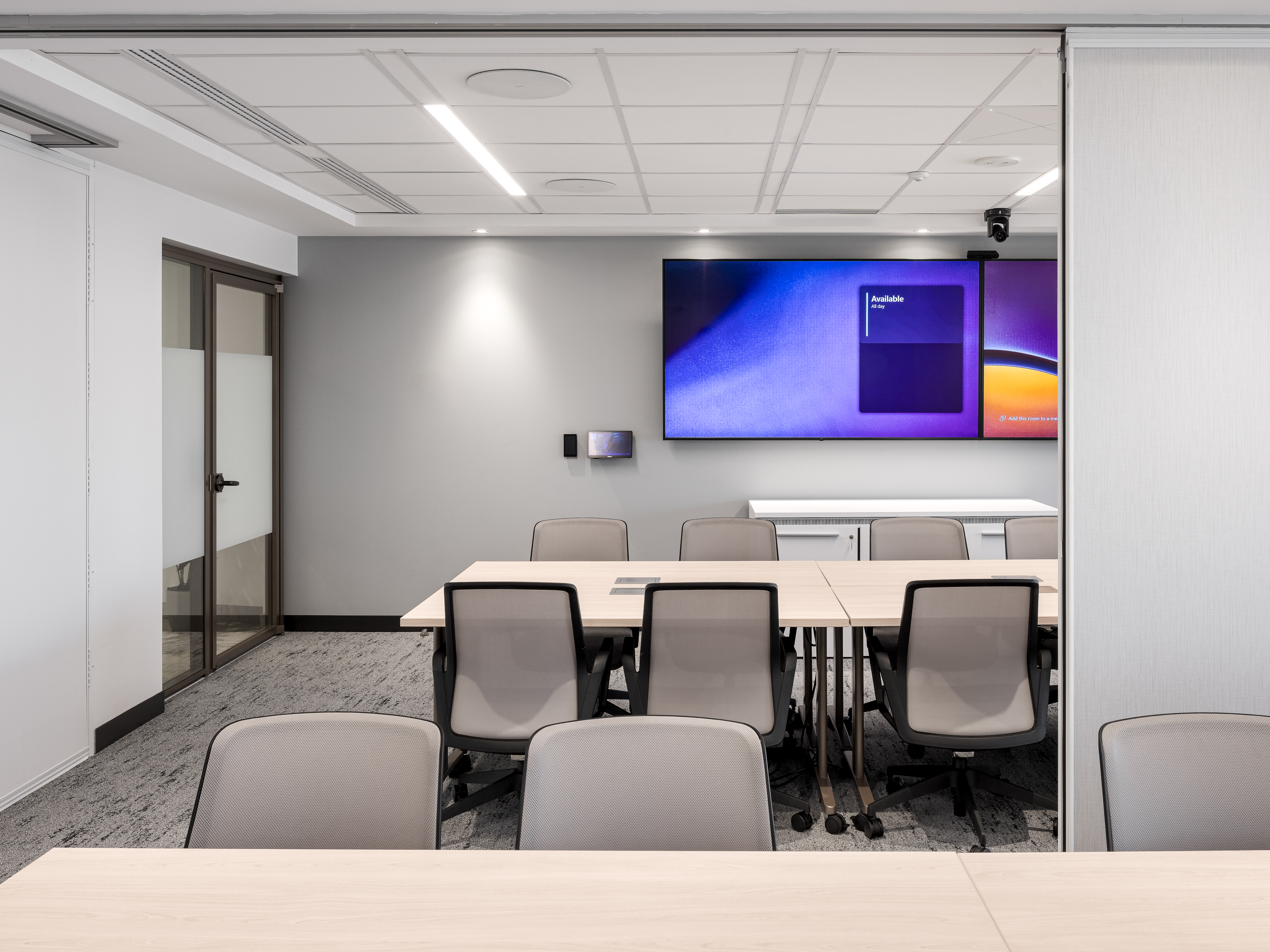 Petite salle de réunion avec table blanche, chaises grises et écran mural, design sobre et lumineux, ACI World, Place Victoria. Photo : TARMAC - Damien Ligiardi