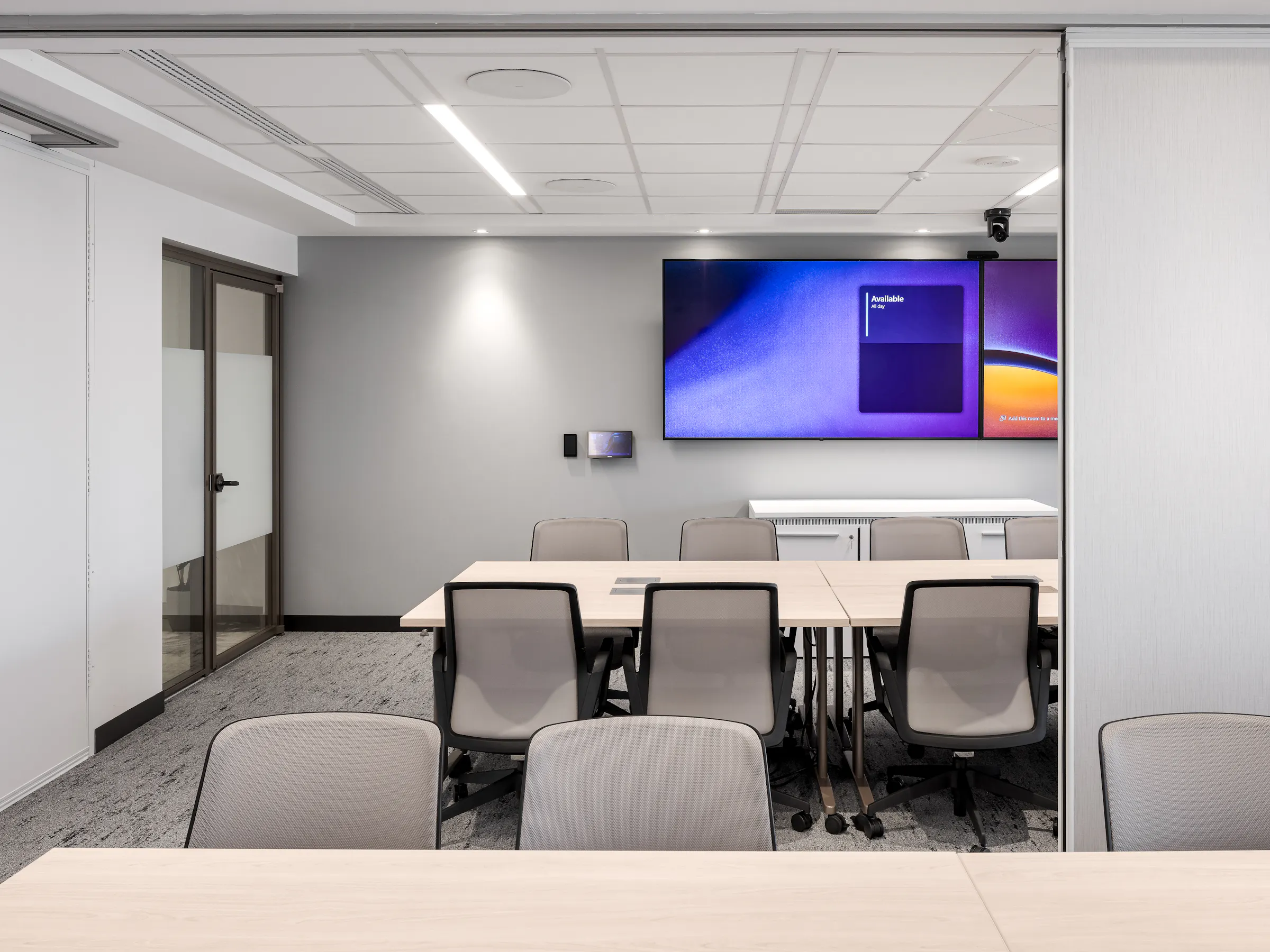 Petite salle de réunion avec table blanche, chaises grises et écran mural, design sobre et lumineux, ACI World, Place Victoria. Photo : TARMAC - Damien Ligiardi