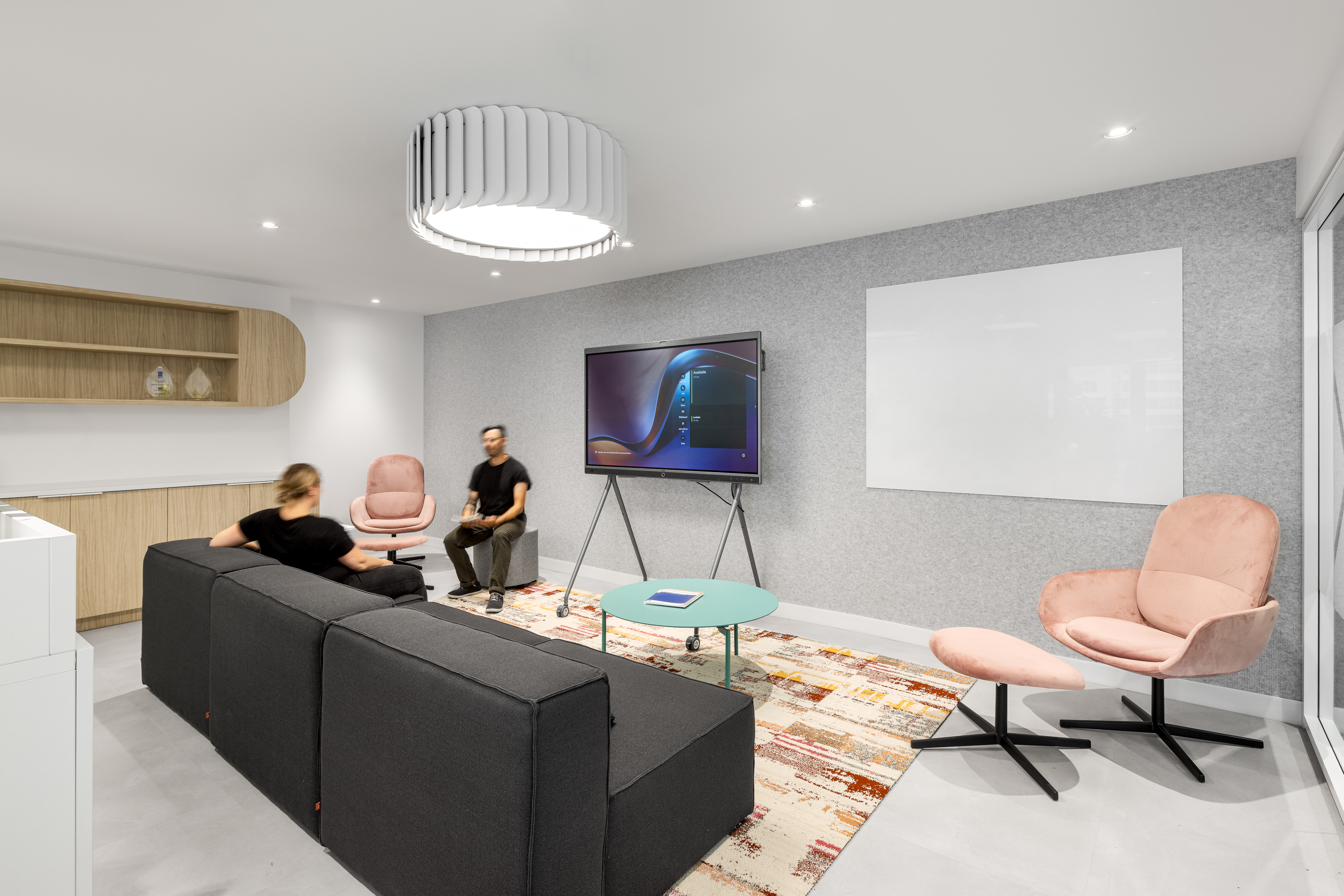 Salle de réunion informelle avec sofas gris foncé et fauteuils roses, dans les bureaux d'ACI World, Place Victoria, Montréal. Photo : TARMAC - Damien Ligiardi