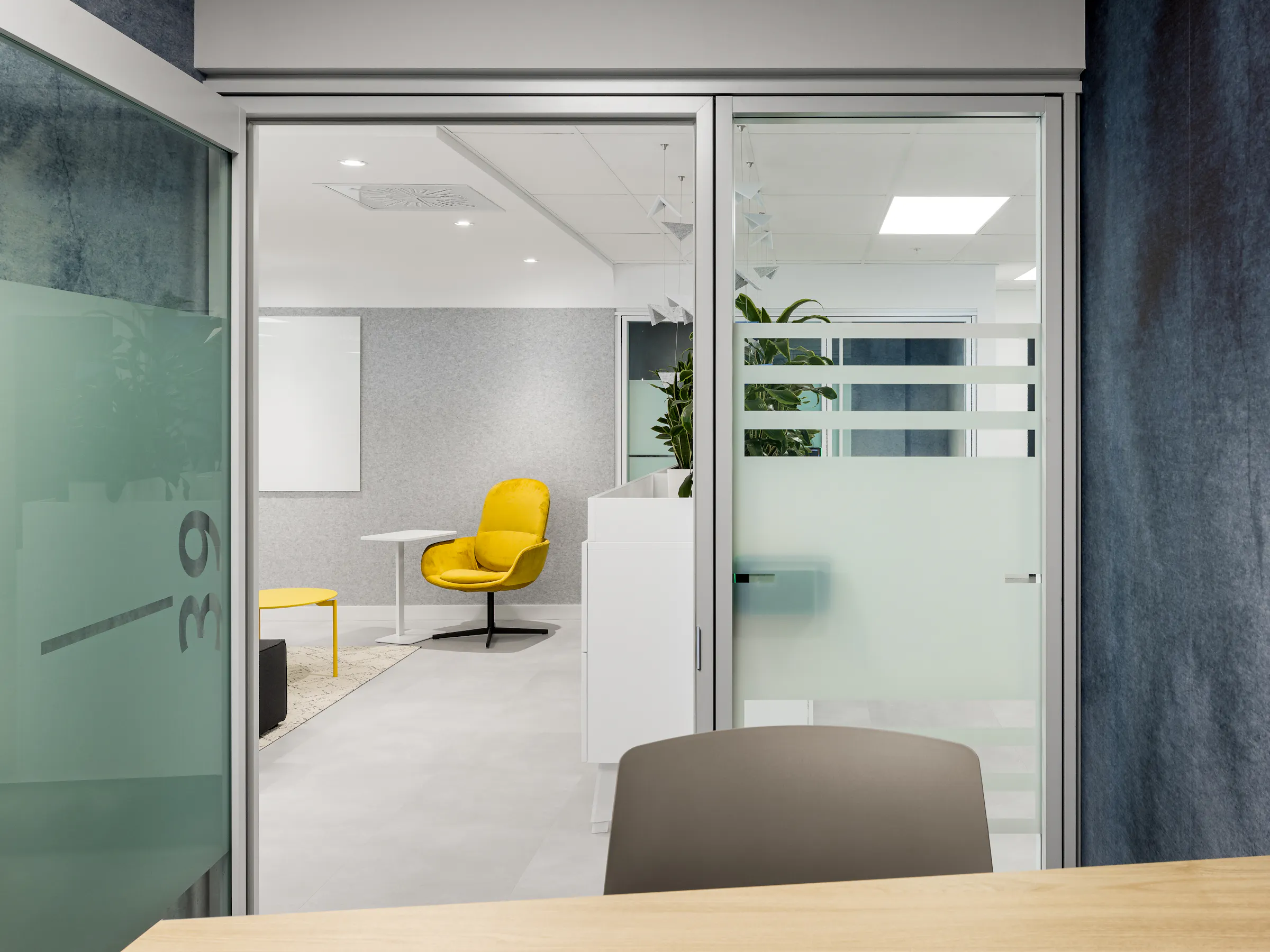 Salle de réunion vitrée avec fauteuil jaune vif, cloisons en verre au motif givré évoquant le tarmac, bureaux ACI World Montréal. Photo : TARMAC - Damien Ligiardi