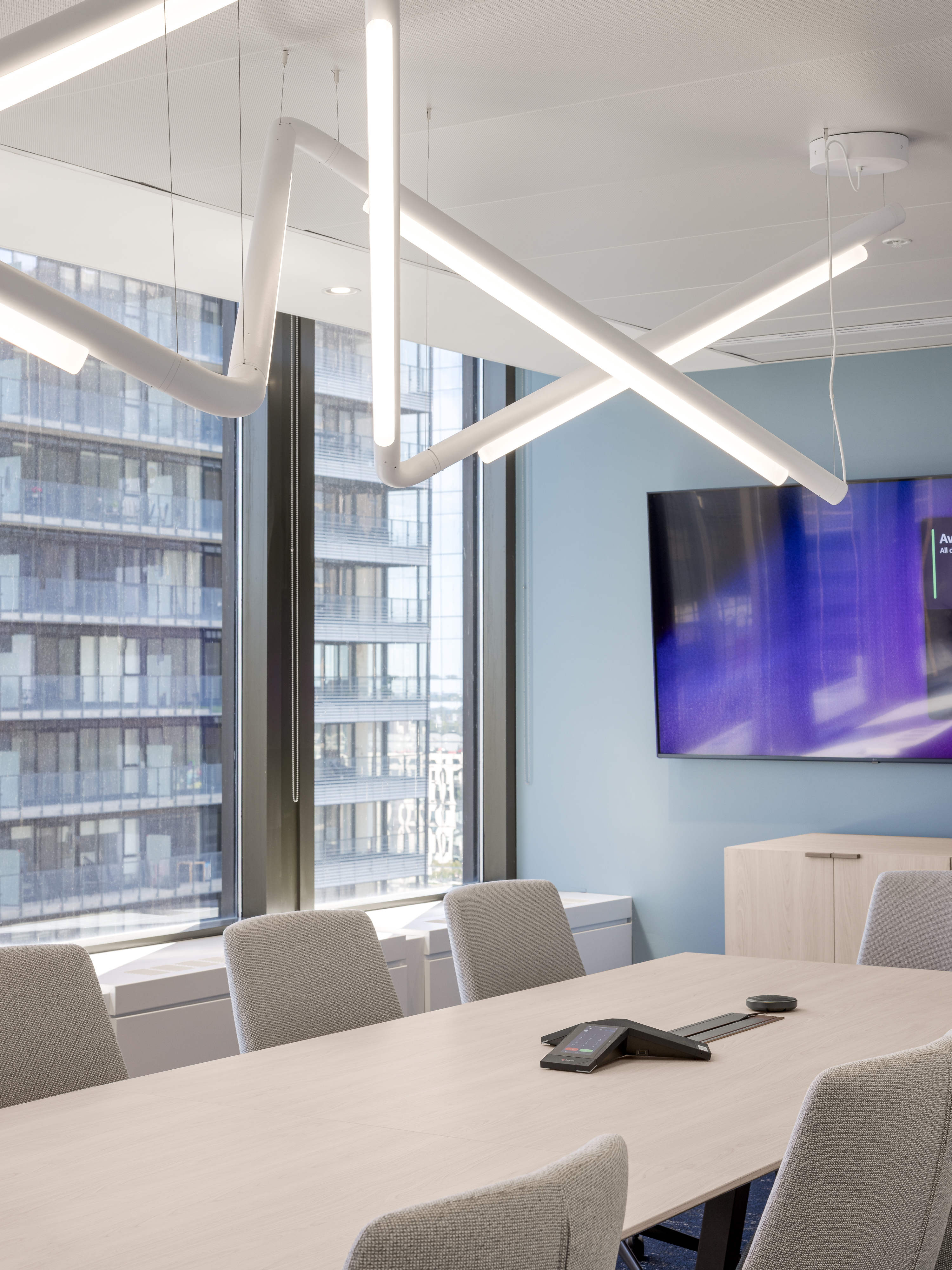 Salle de conférence panoramique avec vue sur les tours du centre-ville de Montréal, éclairage linéaire suspendu en forme de X, bureaux ACI World. Photo : TARMAC - Damien Ligiardi