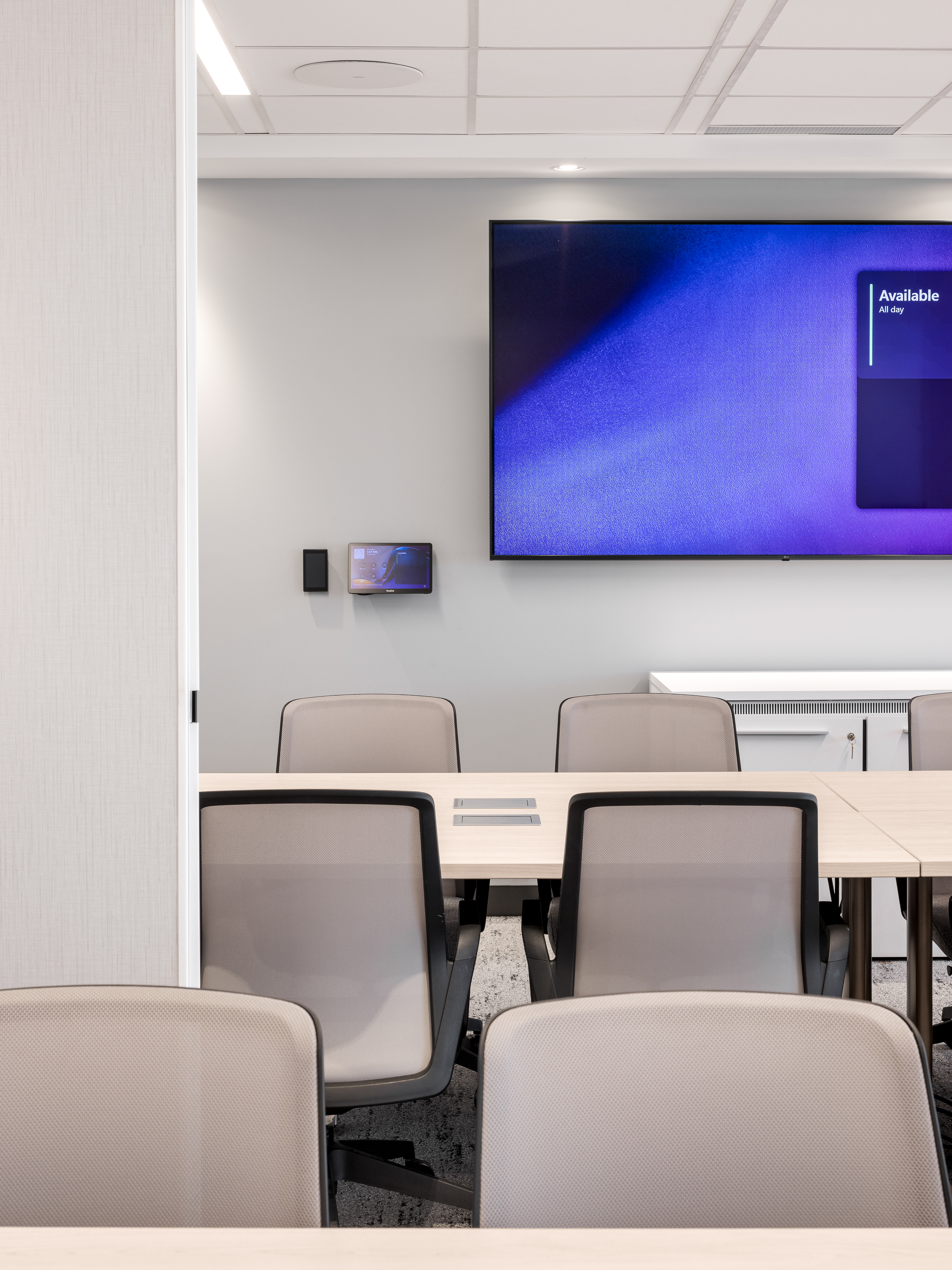 Salle de réunion avec chaises pivotantes grises, grande table et écran mural, atmosphère neutre et fonctionnelle, bureaux ACI World Montréal. Photo : TARMAC - Damien Ligiardi