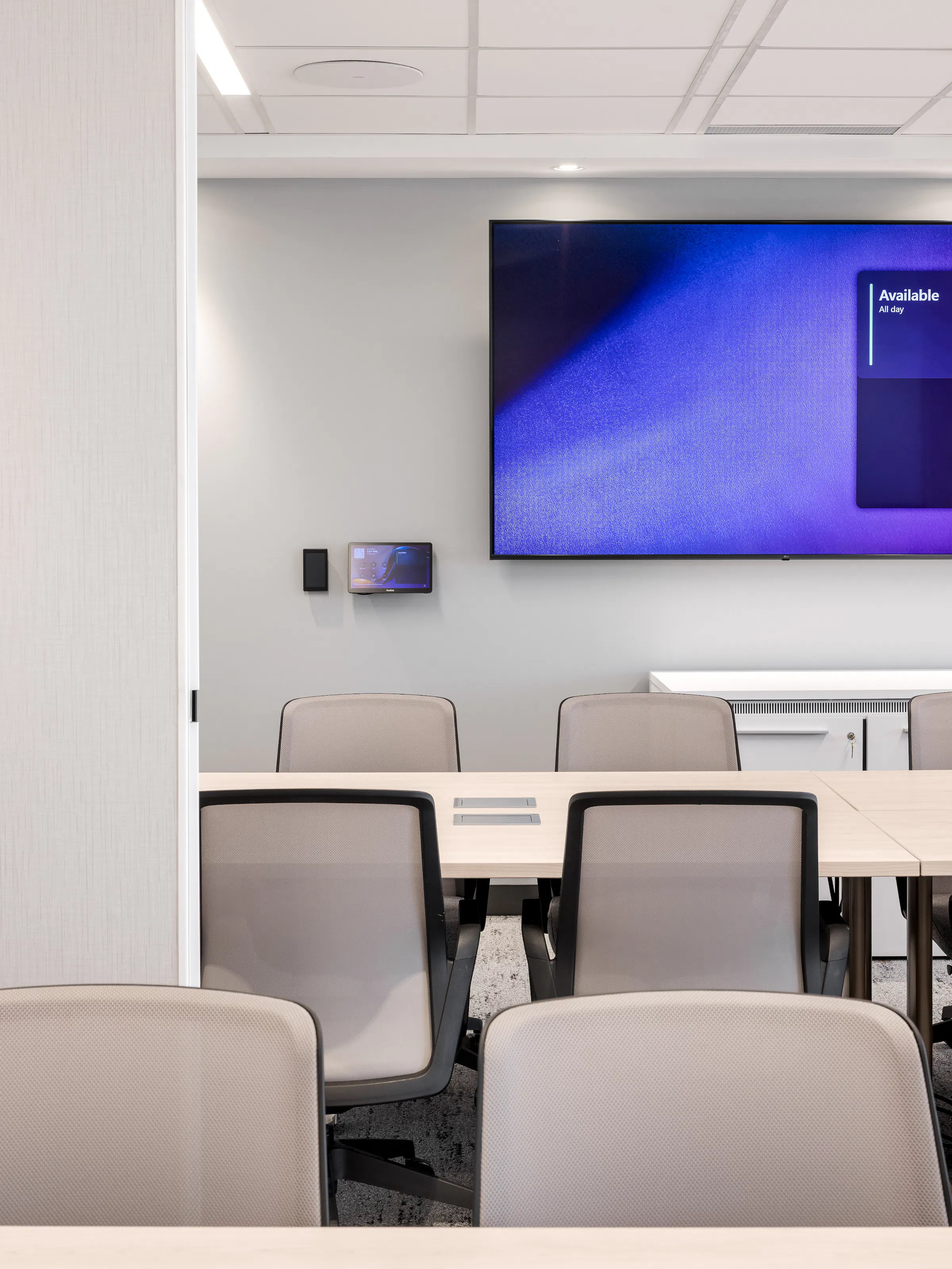 Salle de réunion avec chaises pivotantes grises, grande table et écran mural, atmosphère neutre et fonctionnelle, bureaux ACI World Montréal. Photo : TARMAC - Damien Ligiardi