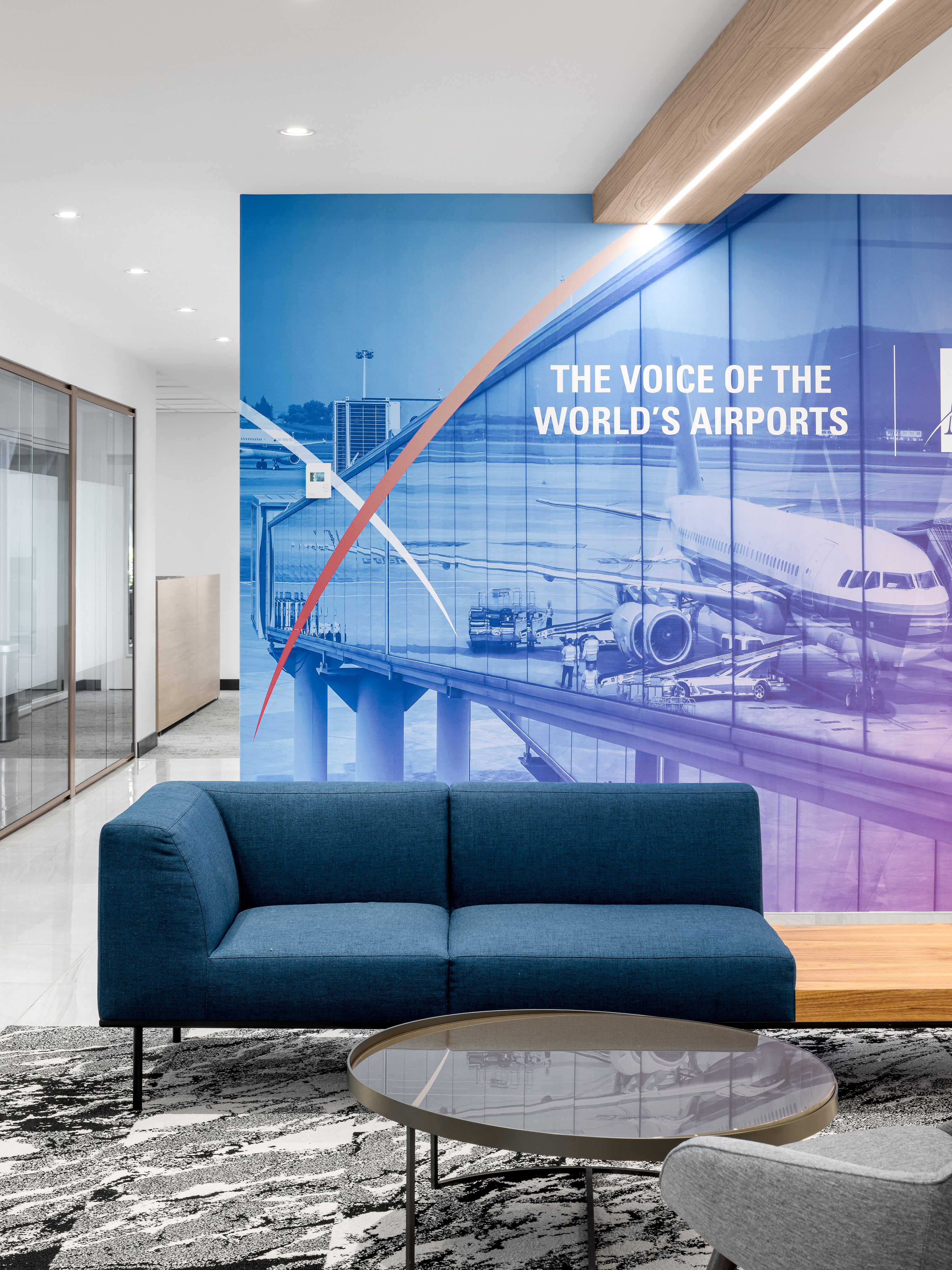 Espace d'attente avec canapé bleu sarcelle et murale "The Voice of the World's Airports", réception des bureaux d'ACI World à la Place Victoria, Montréal. Photo : TARMAC - Damien Ligiardi