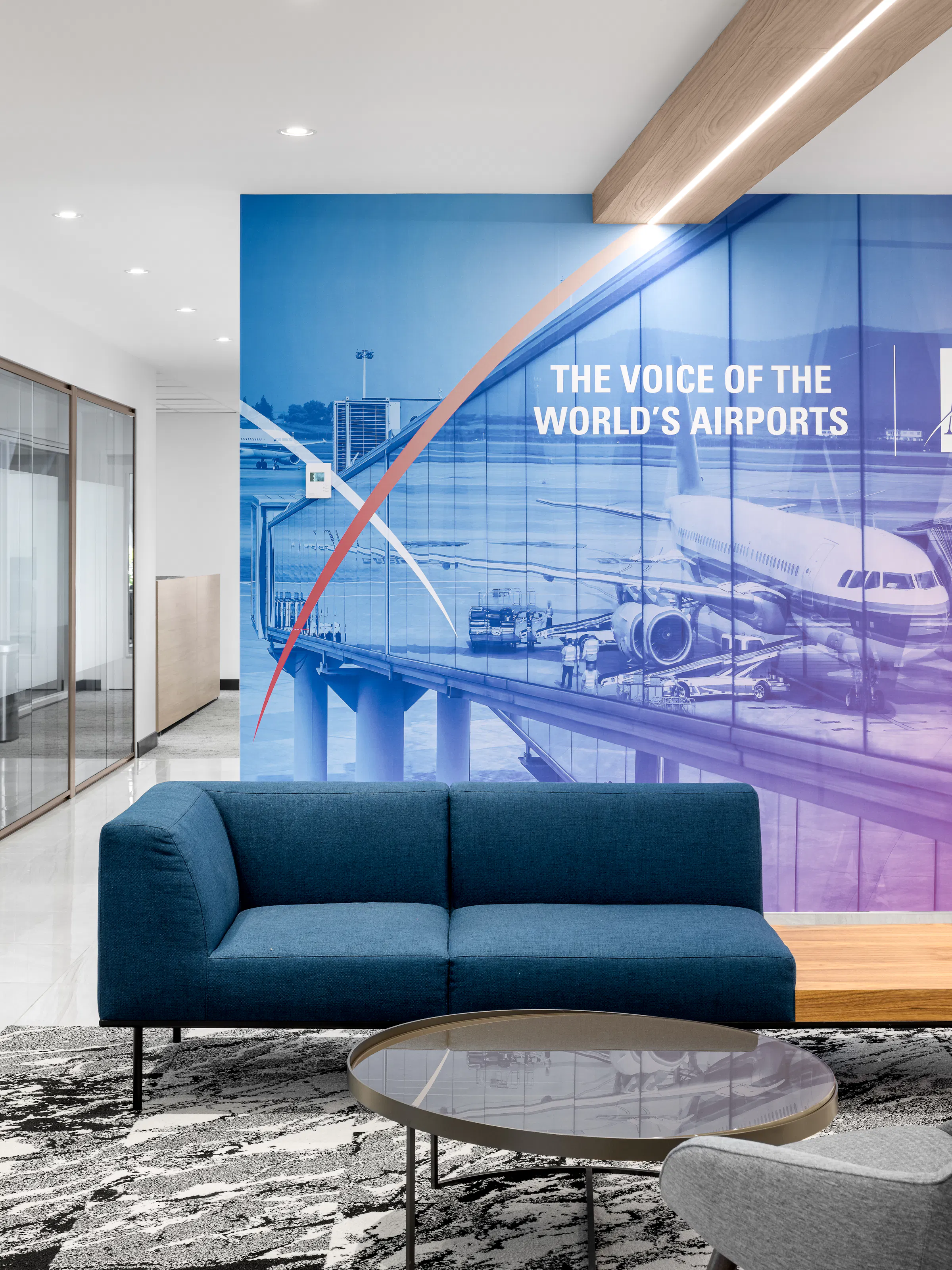 Espace d'attente avec canapé bleu sarcelle et murale "The Voice of the World's Airports", réception des bureaux d'ACI World à la Place Victoria, Montréal. Photo : TARMAC - Damien Ligiardi