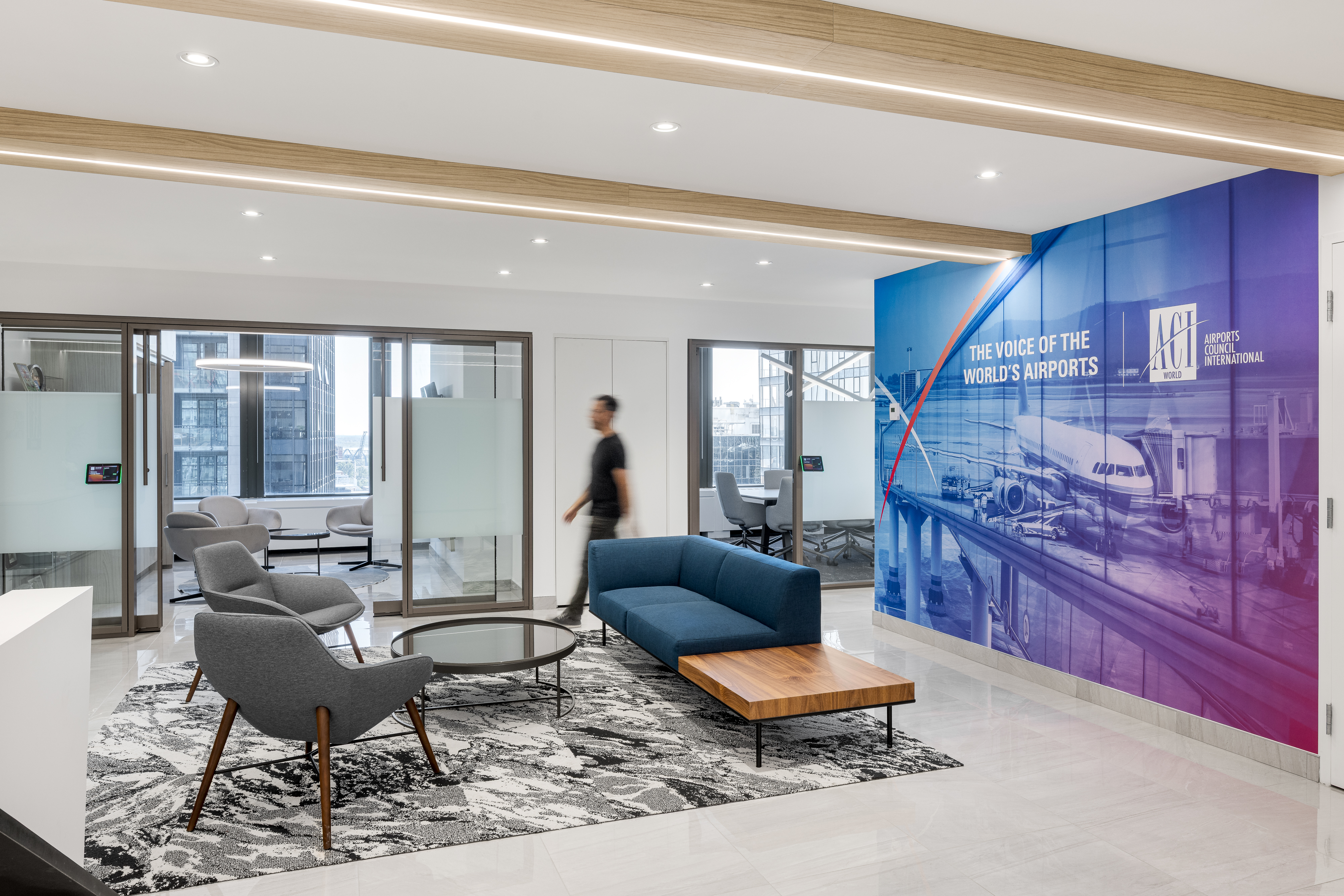 Réception des bureaux d'ACI World à la Place Victoria, avec murale grand format "The Voice of the World's Airports", canapé bleu, fauteuils gris et poutres en bois rappelant la cabine d'avion. Photo : TARMAC - Damien Ligiardi
