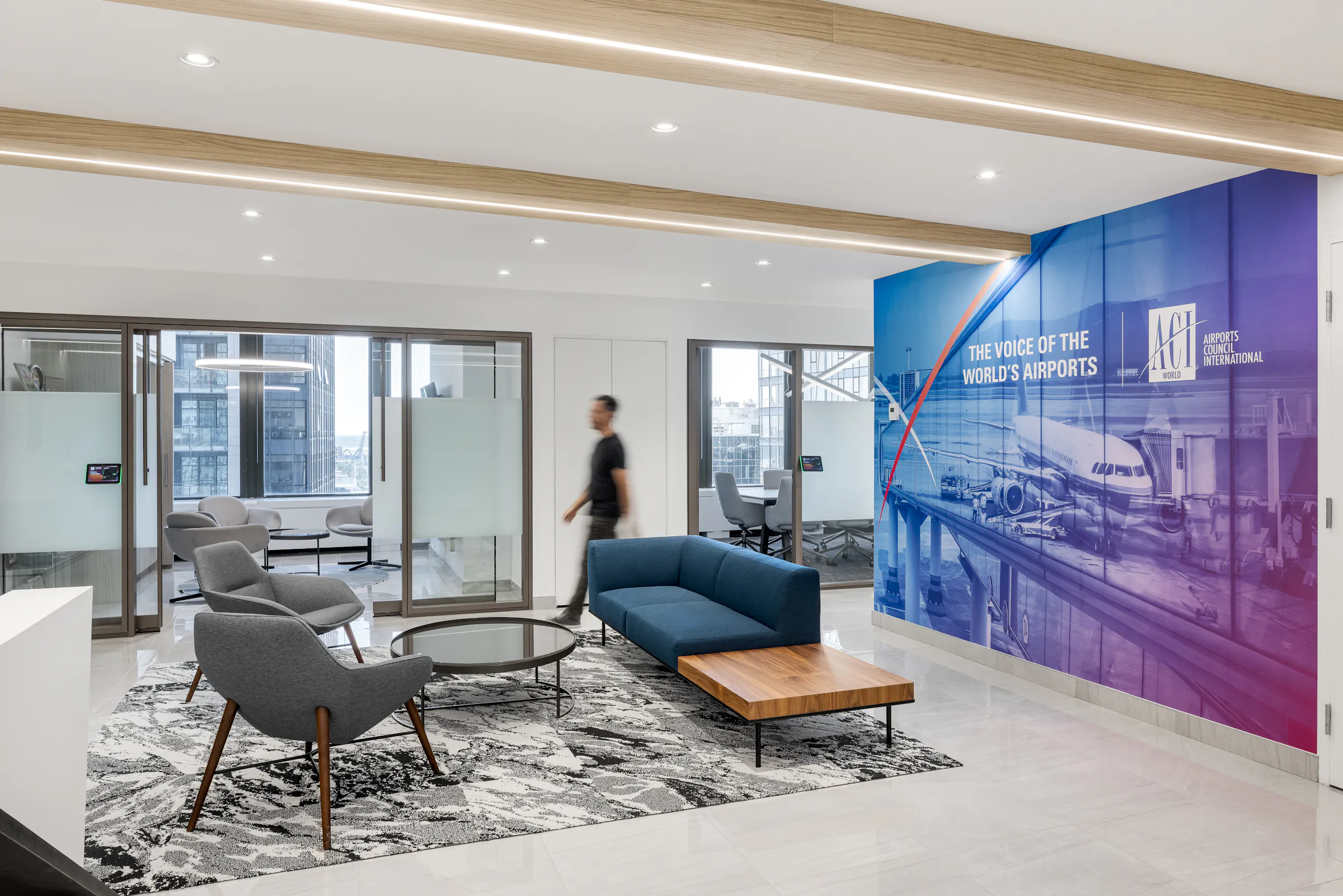 Réception des bureaux d'ACI World à la Place Victoria, avec murale grand format "The Voice of the World's Airports", canapé bleu, fauteuils gris et poutres en bois rappelant la cabine d'avion. Photo : TARMAC - Damien Ligiardi