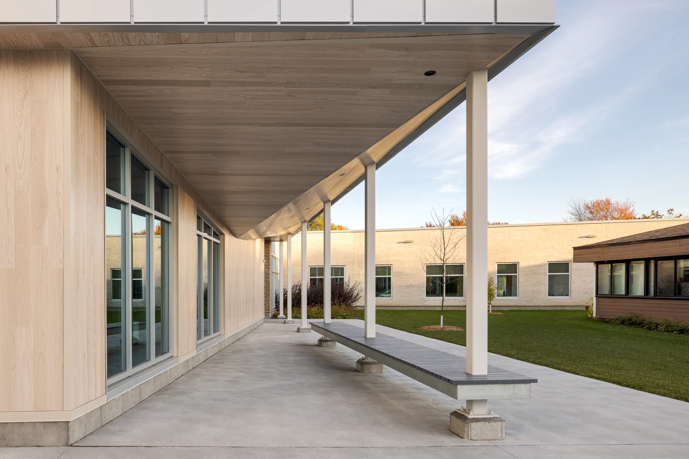 An exterior covered walkway with a wood and concrete structure connects the courtyard spaces, bathed in natural light. Photo: TARMAC - Damien Ligiardi