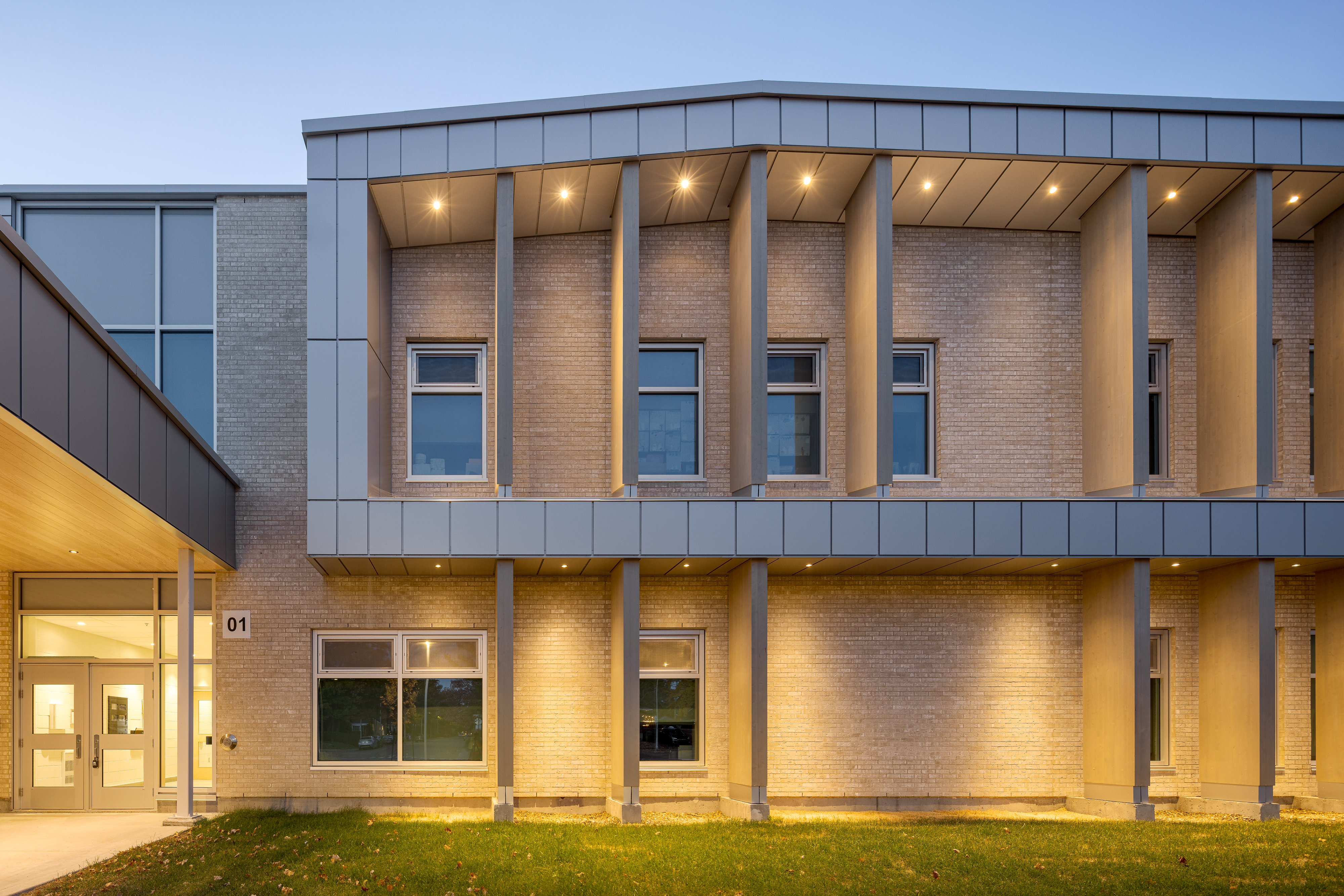 Side facade of the new wing at dusk, columns and windows illuminated from within. Photo: TARMAC - Damien Ligiardi