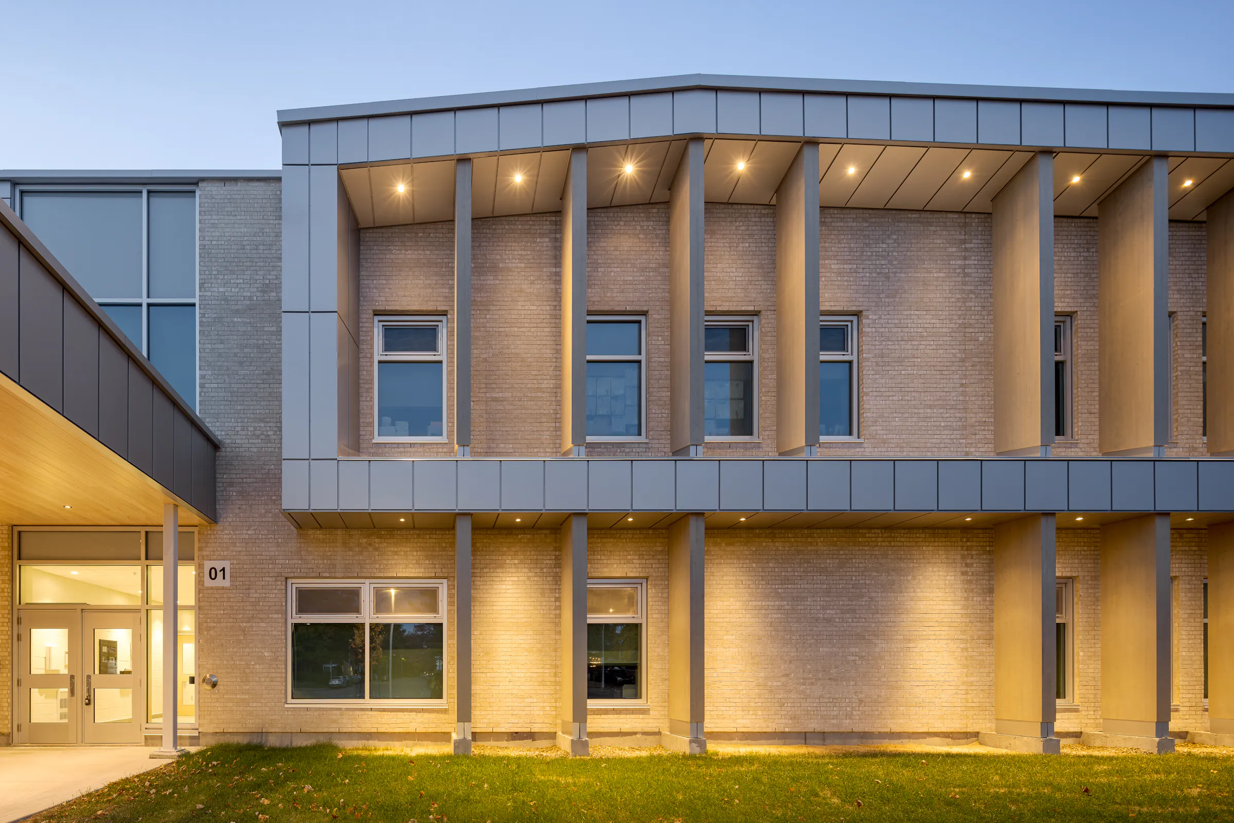 Side facade of the new wing at dusk, columns and windows illuminated from within. Photo: TARMAC - Damien Ligiardi