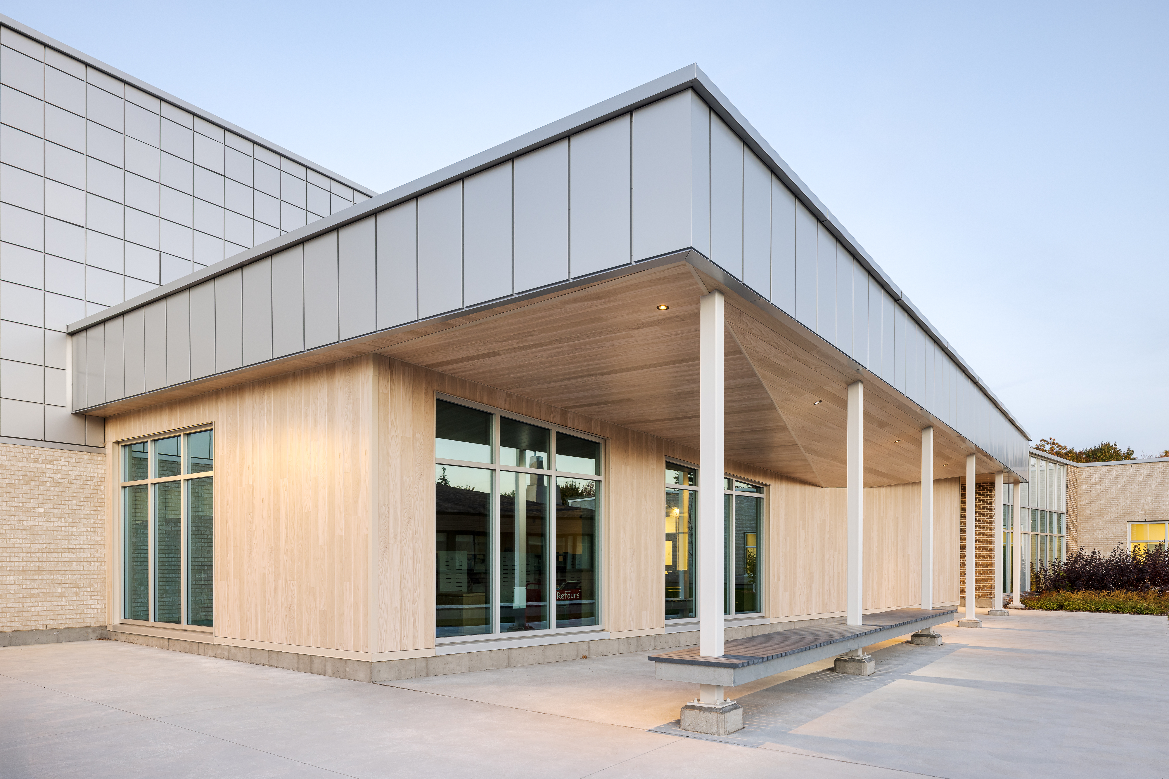 Entrance covered with a wooden structure, integrated lighting under the roof, brick facade in the background. Photo: TARMAC - Damien Ligiardi