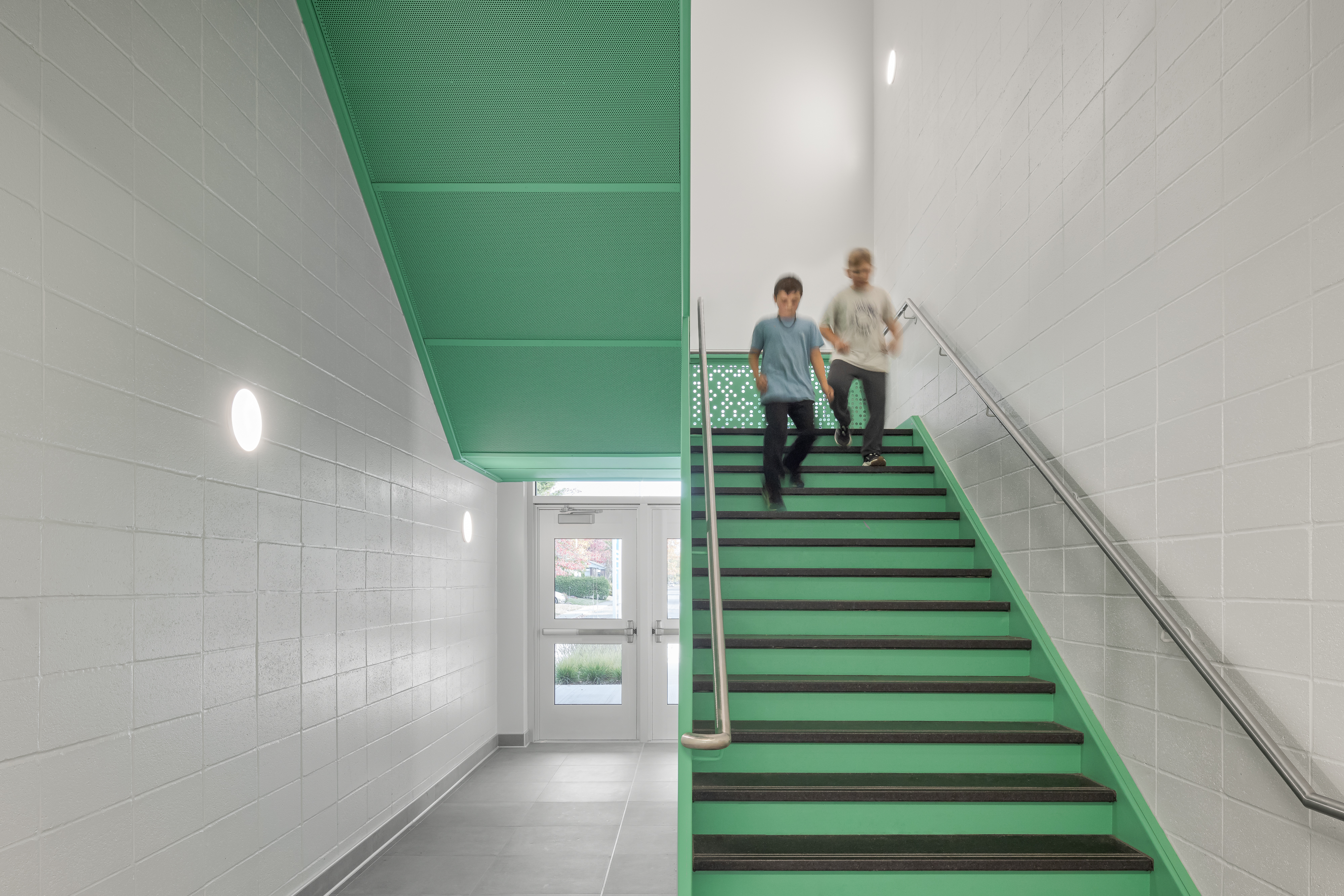 Stairwell with green perforated metal railing, students moving about, contemporary design. Photo: TARMAC - Damien Ligiardi