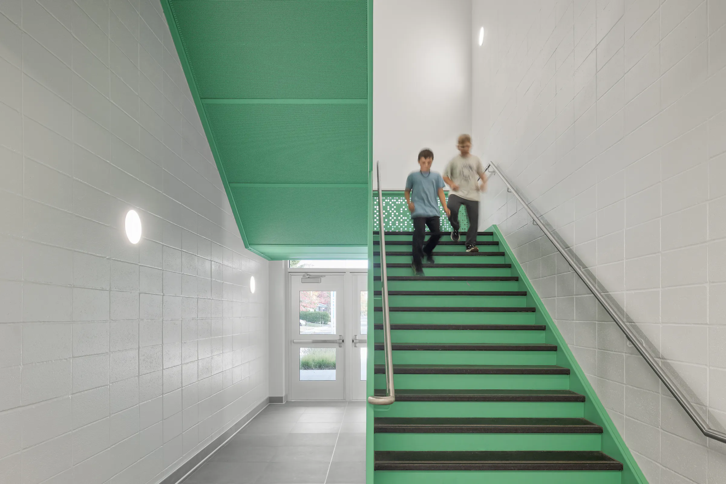 Stairwell with green perforated metal railing, students moving about, contemporary design. Photo: TARMAC - Damien Ligiardi