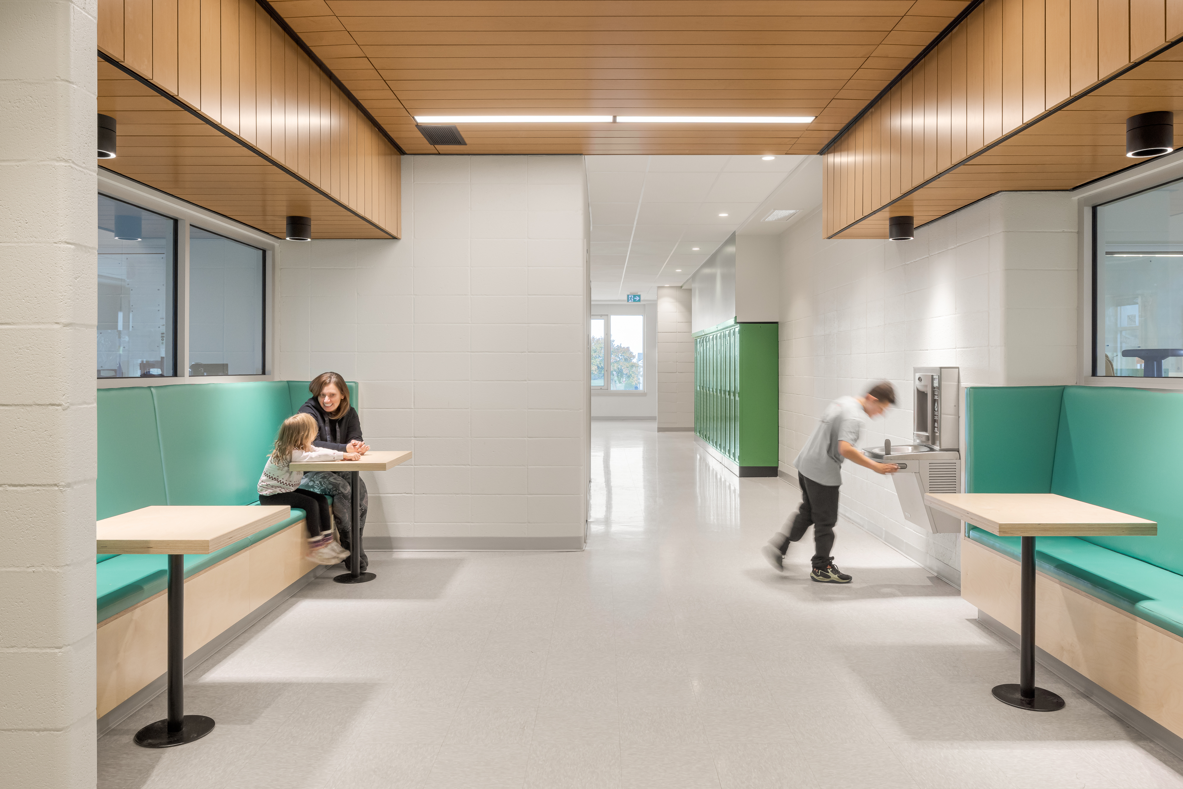 Collaborative workspace in the corridor, benches and high tables, wooden lockers, and green accents. Photo: TARMAC - Damien Ligiardi