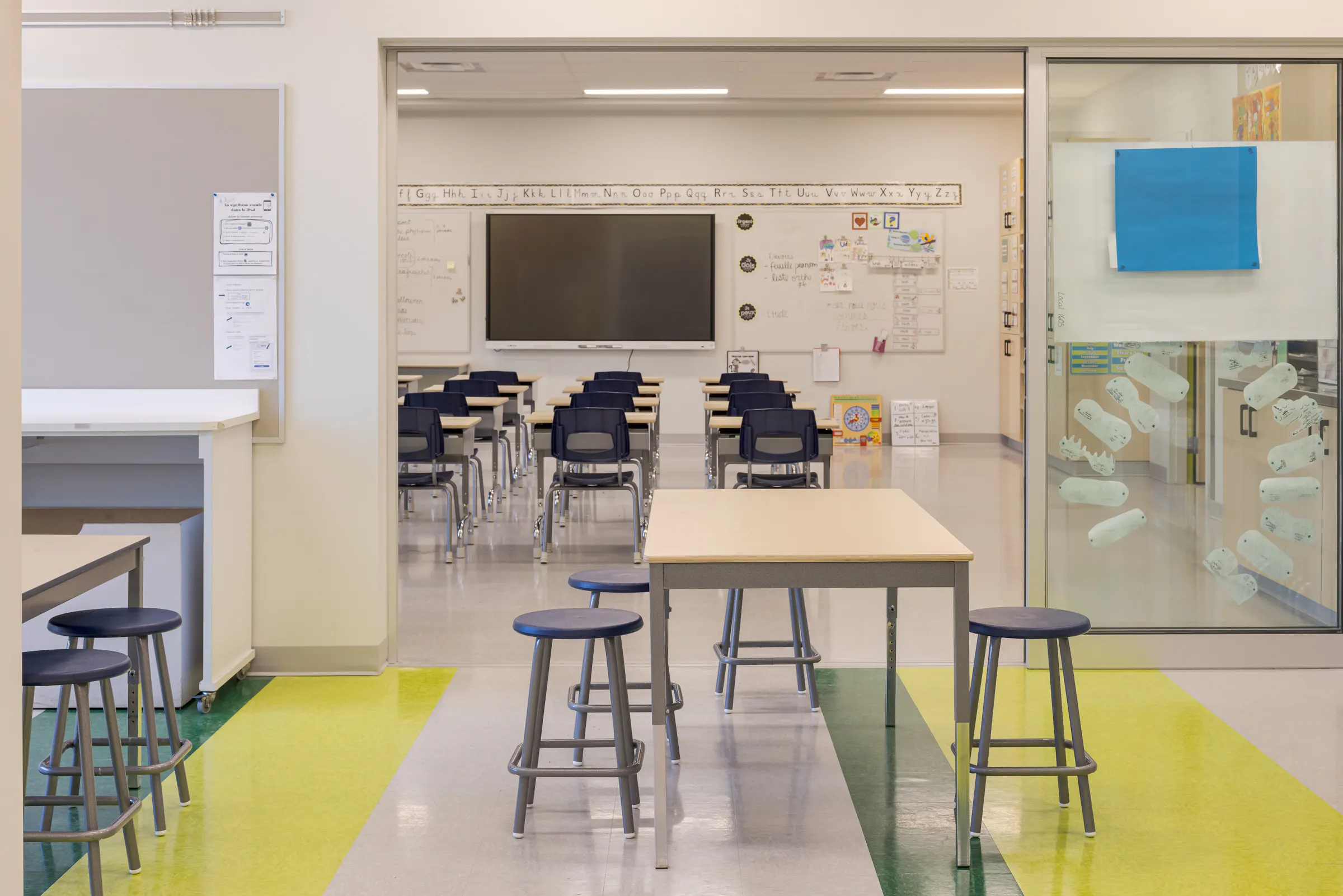 Classroom with flexible furniture, interactive whiteboard, and rows of colorful lockers visible through the glass door. Photo: TARMAC - Damien Ligiardi