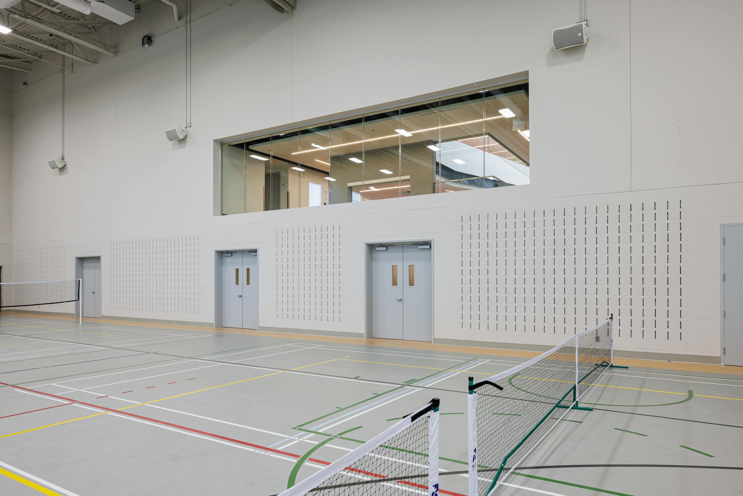 Photographie d'un terrain sportif dans un gymnase.
La surface et grise et les lignes multicolors.
