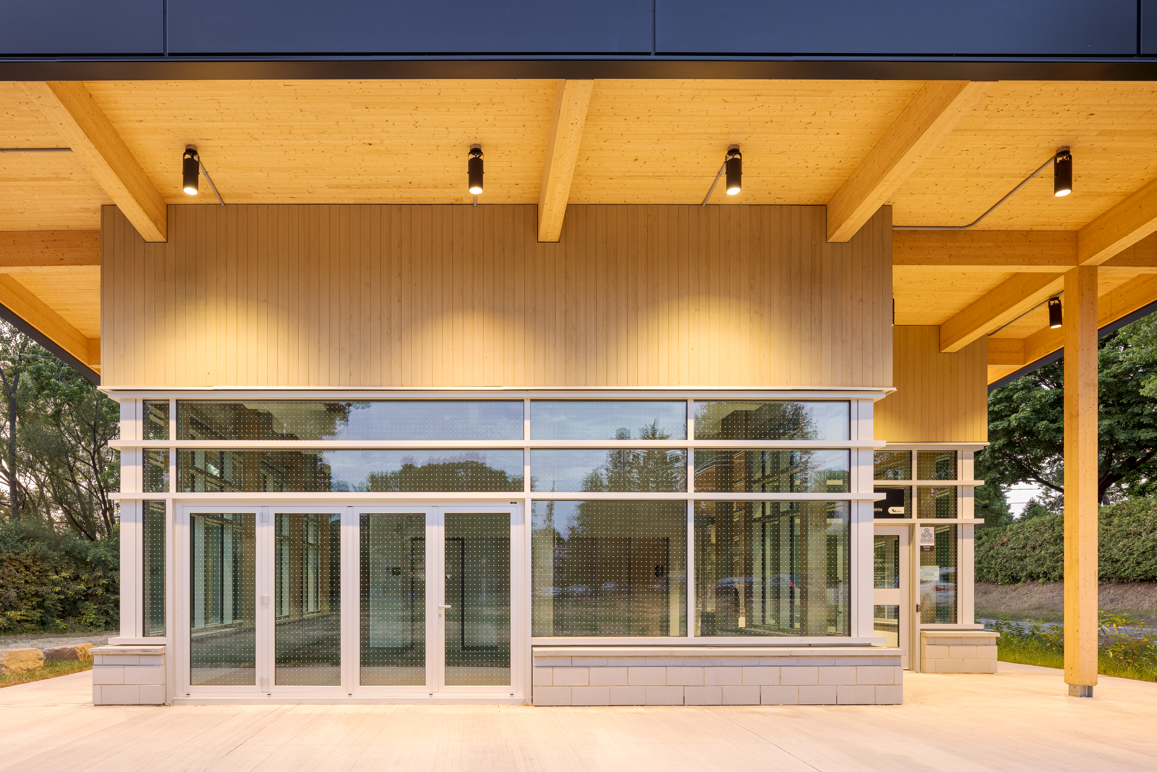 Photographie du plafond en bois lamellé du chalet, mettant en valeur la charpente exposée et l'auvent en porte-à-faux au coucher du soleil.