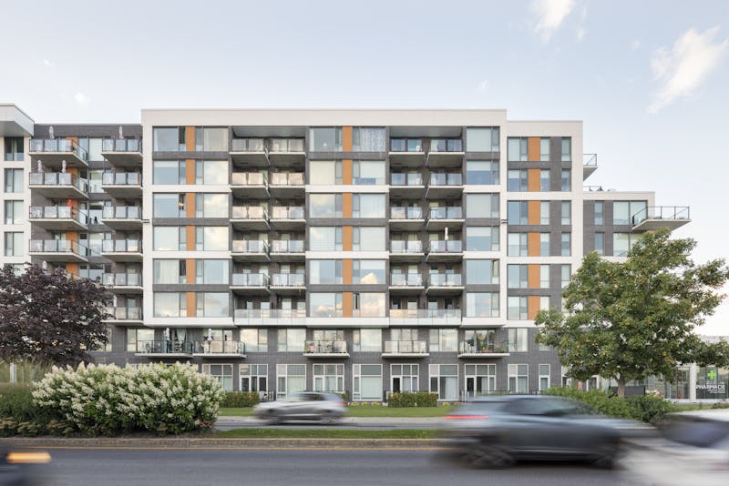 Photographie architecturale de la façade d'une bâtisse de 8 étages avec des voiture en mouvement au premier plan.