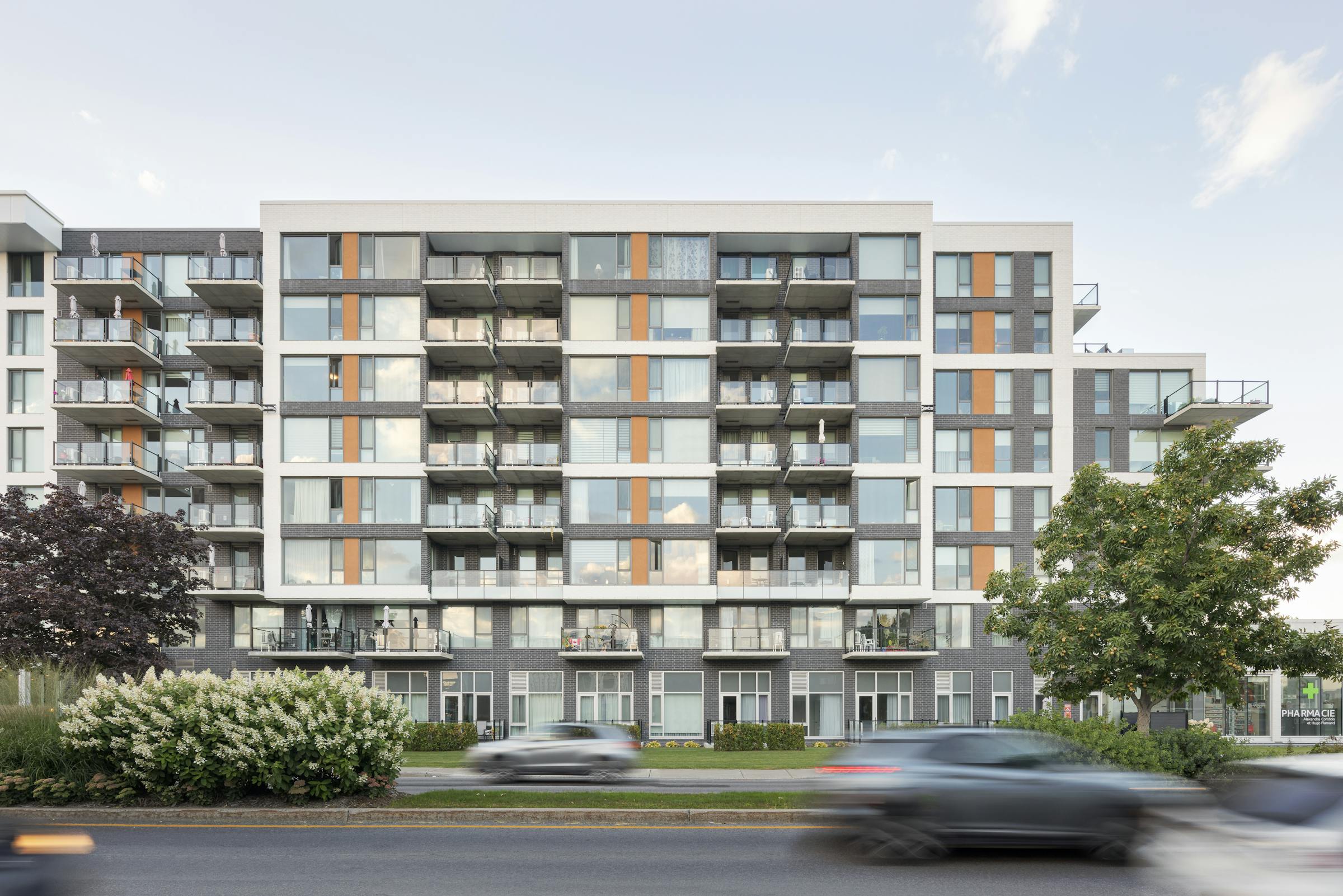 Architectural photograph of the facade of an 8-story building with moving cars in the foreground.