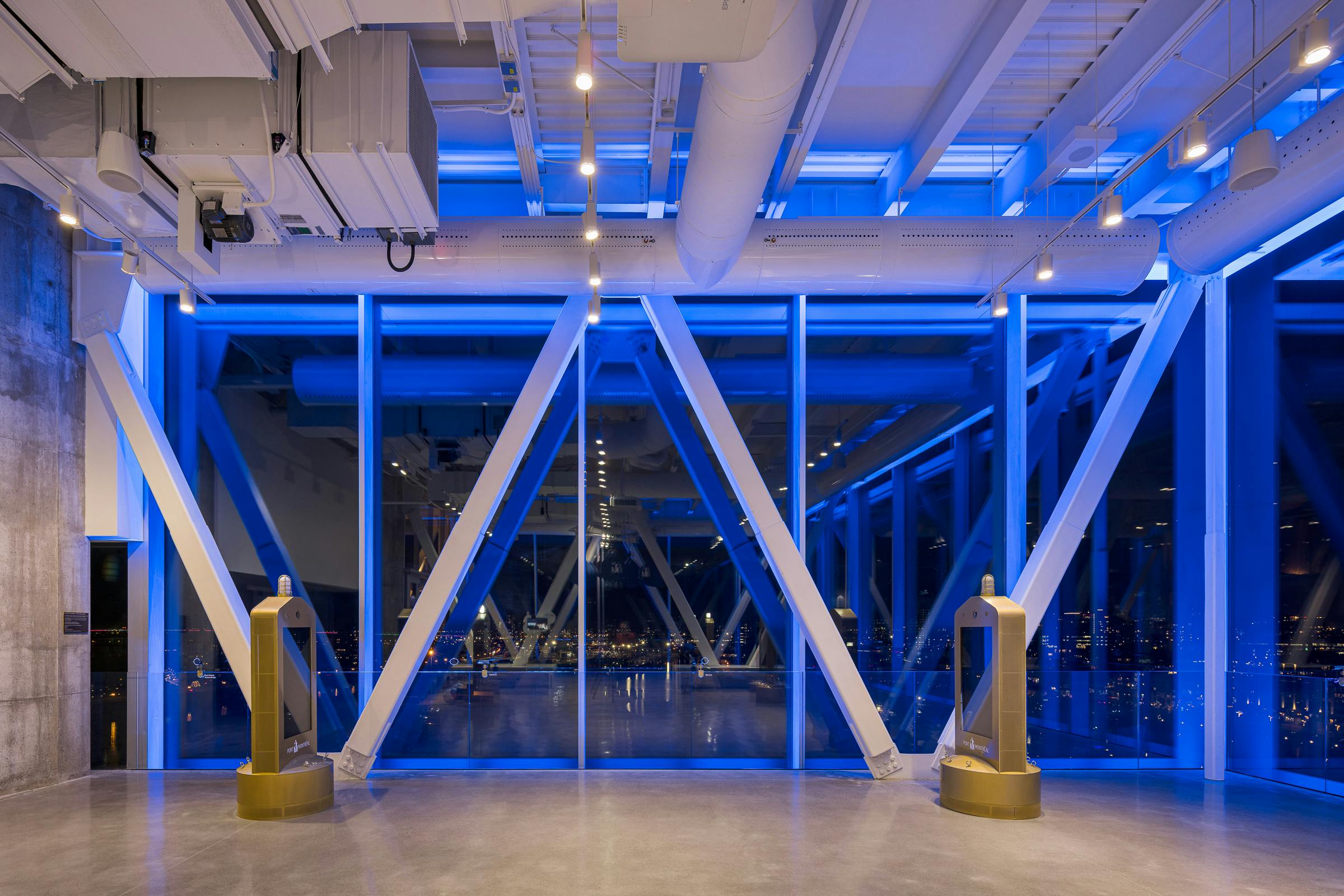 Photograph of an observation platform over the city of Montreal. It's dark and the blue lighting in the room is dominant.
