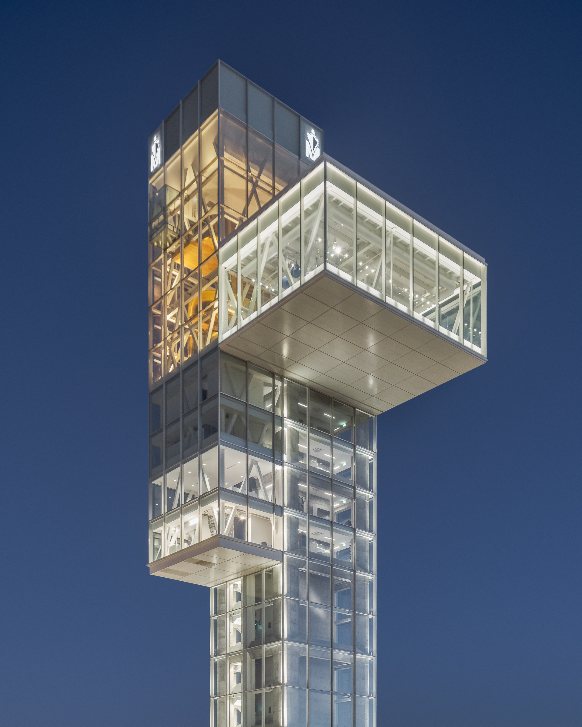 Night photograph of the cantilevered observation room taken from a low angle. Midnight blue sky and dominant artificial lighting.