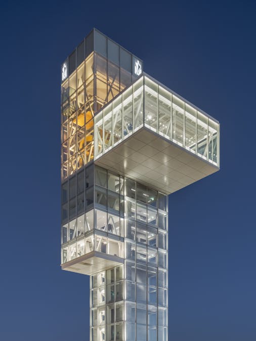 Night photograph of the cantilevered observation room taken from a low angle. Midnight blue sky and dominant artificial lighting.