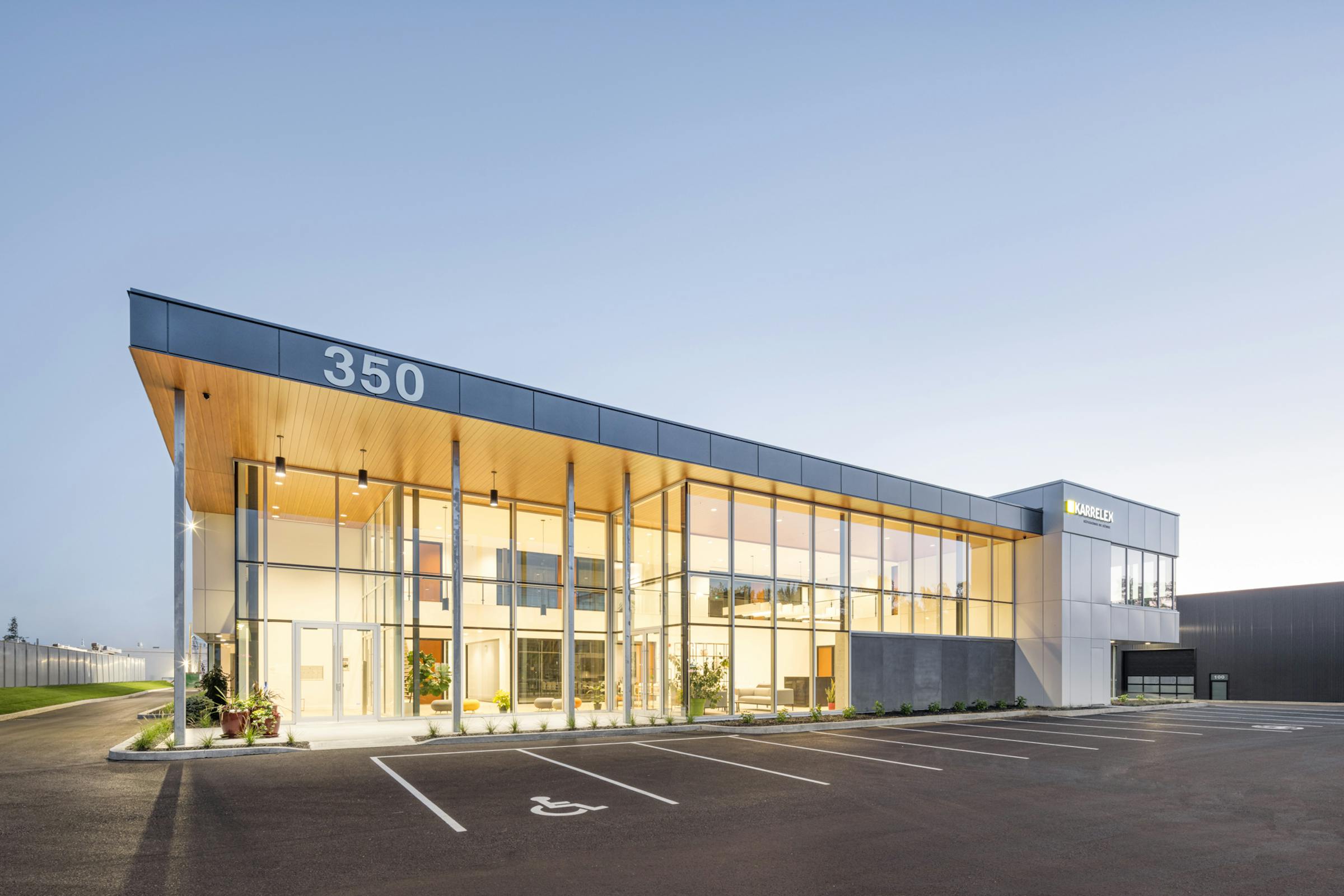 Architectural photograph of a 3/4 commercial building with an empty parking lot in the foreground. Artificial lighting is predominant.