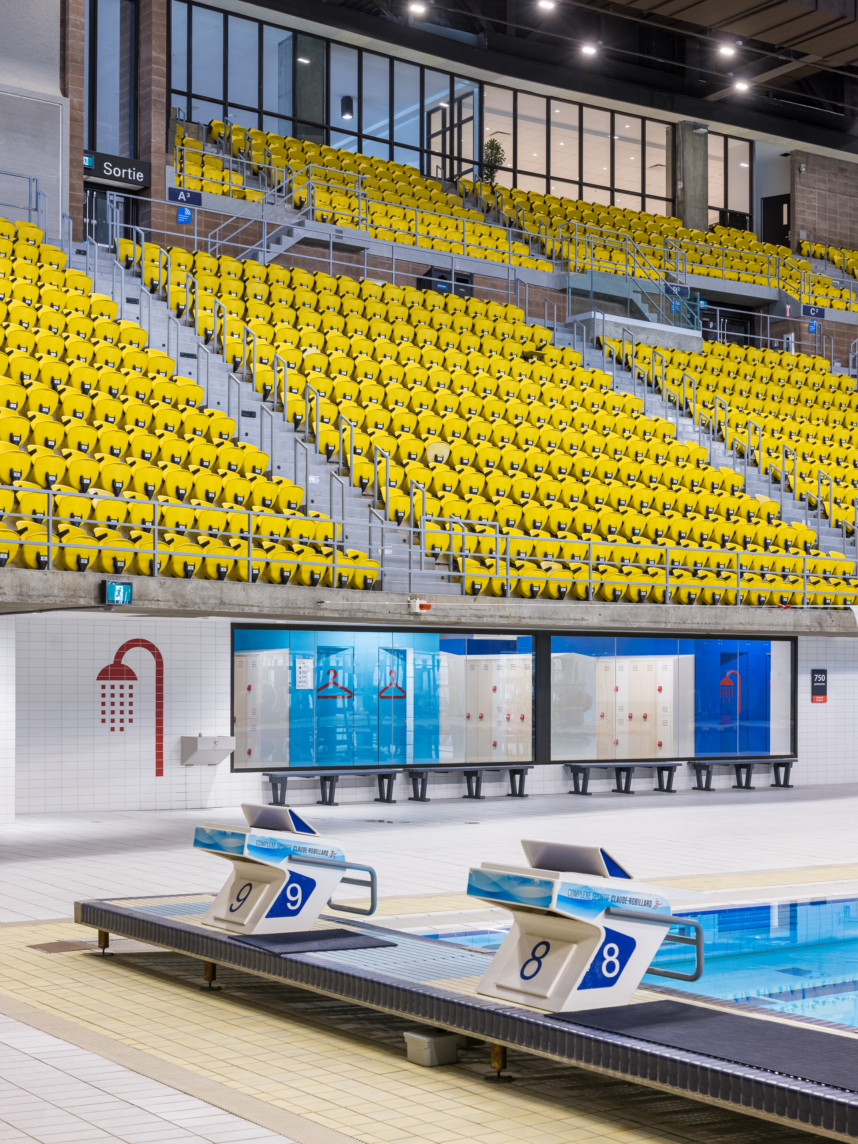 Architectural photograph of the yellow bleachers overlooking the swimming pool of the sports complex.