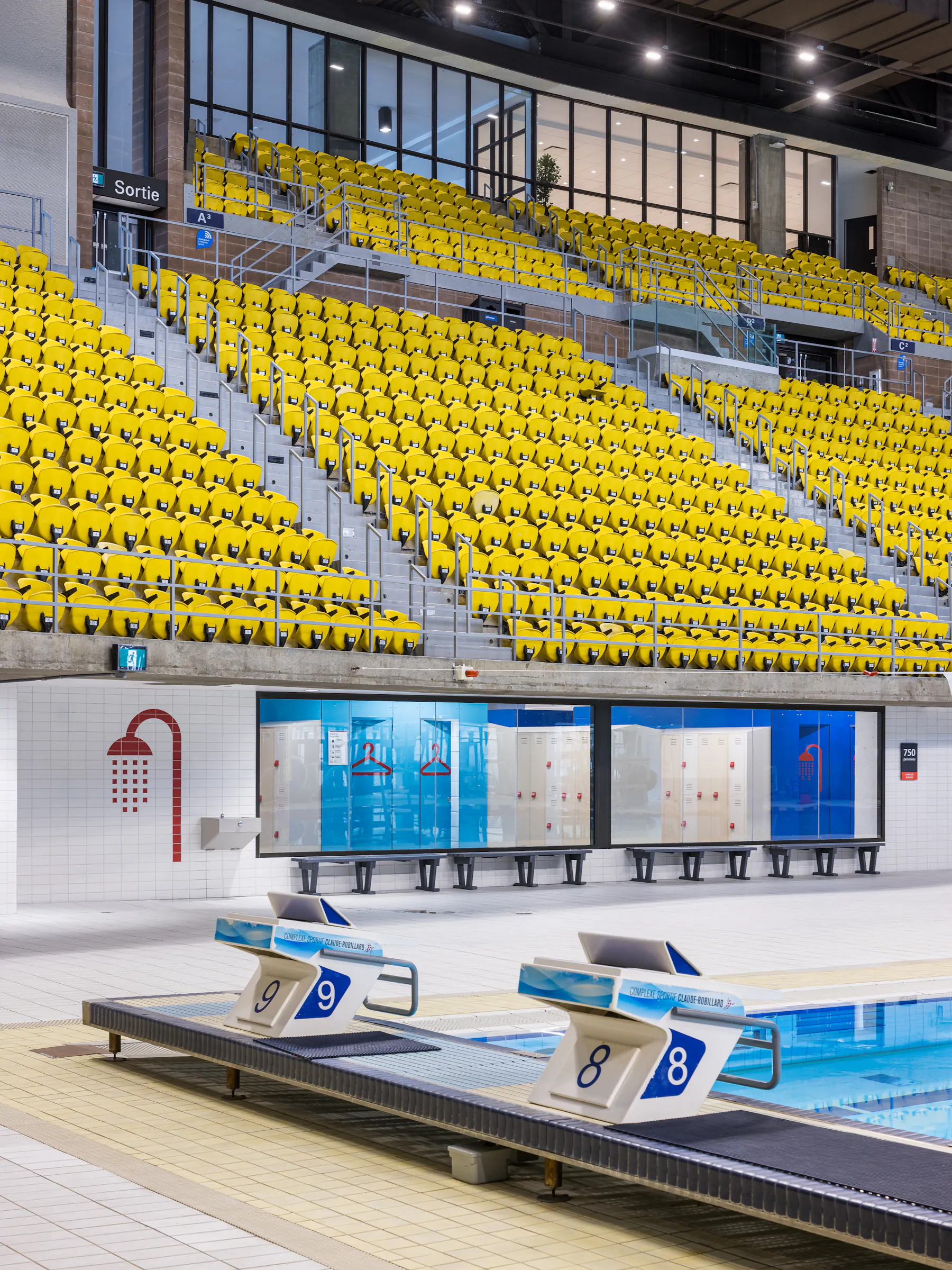 Architectural photograph of the yellow bleachers overlooking the swimming pool of the sports complex.