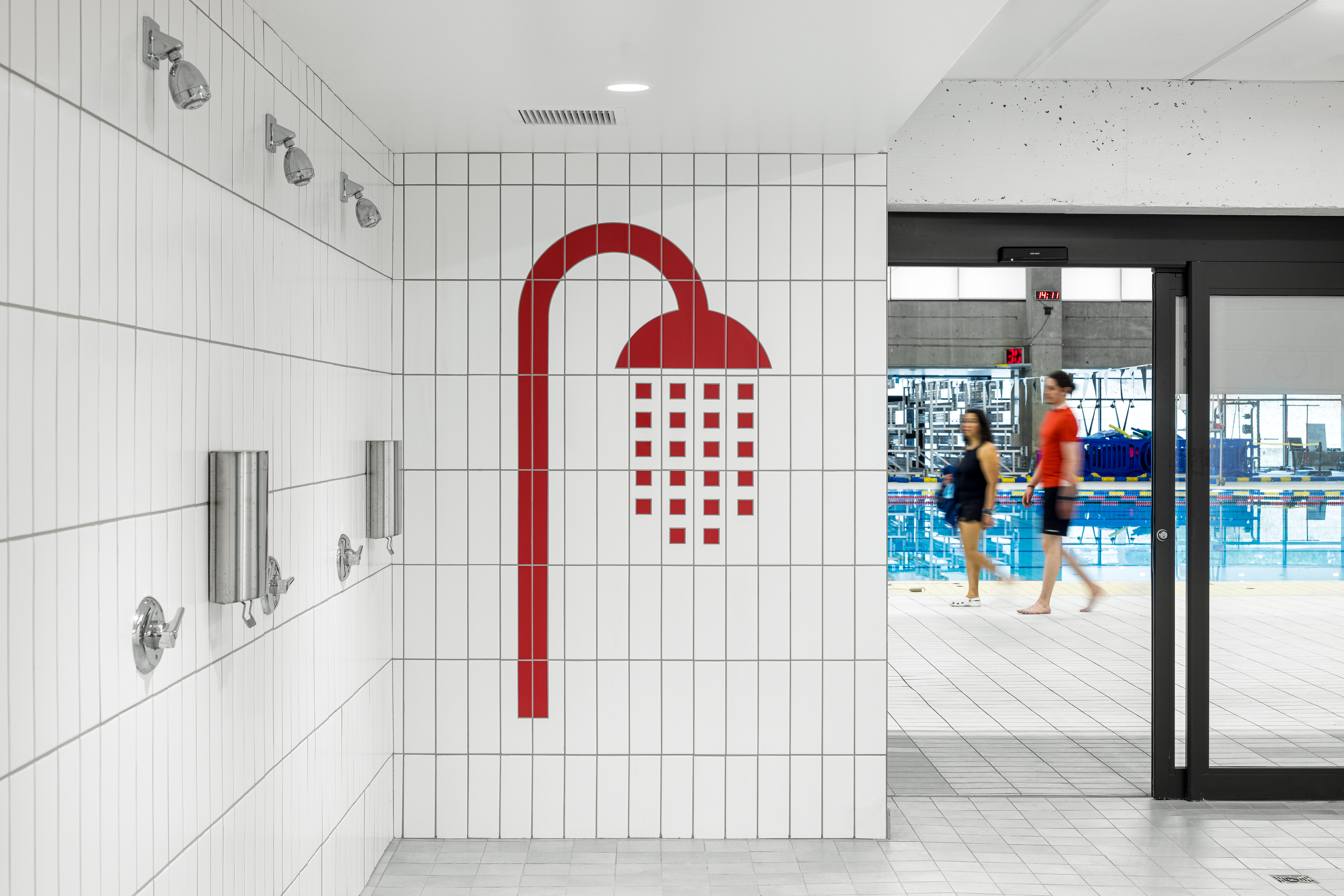 Architectural photograph of a bathroom, white tiled showers with red pictograms in a universal changing room.