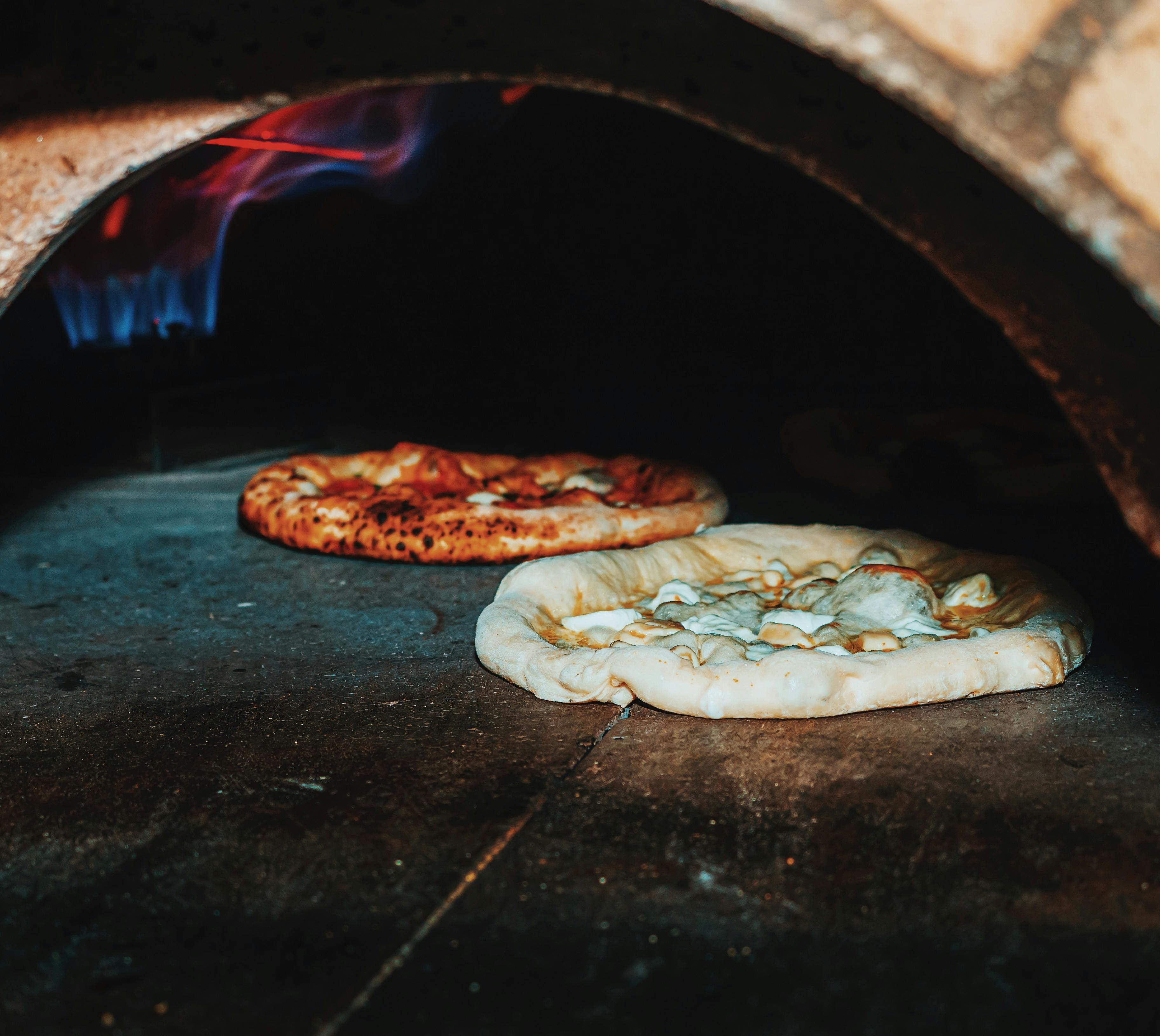 Two pizzas cooking in the 800 degree brick oven