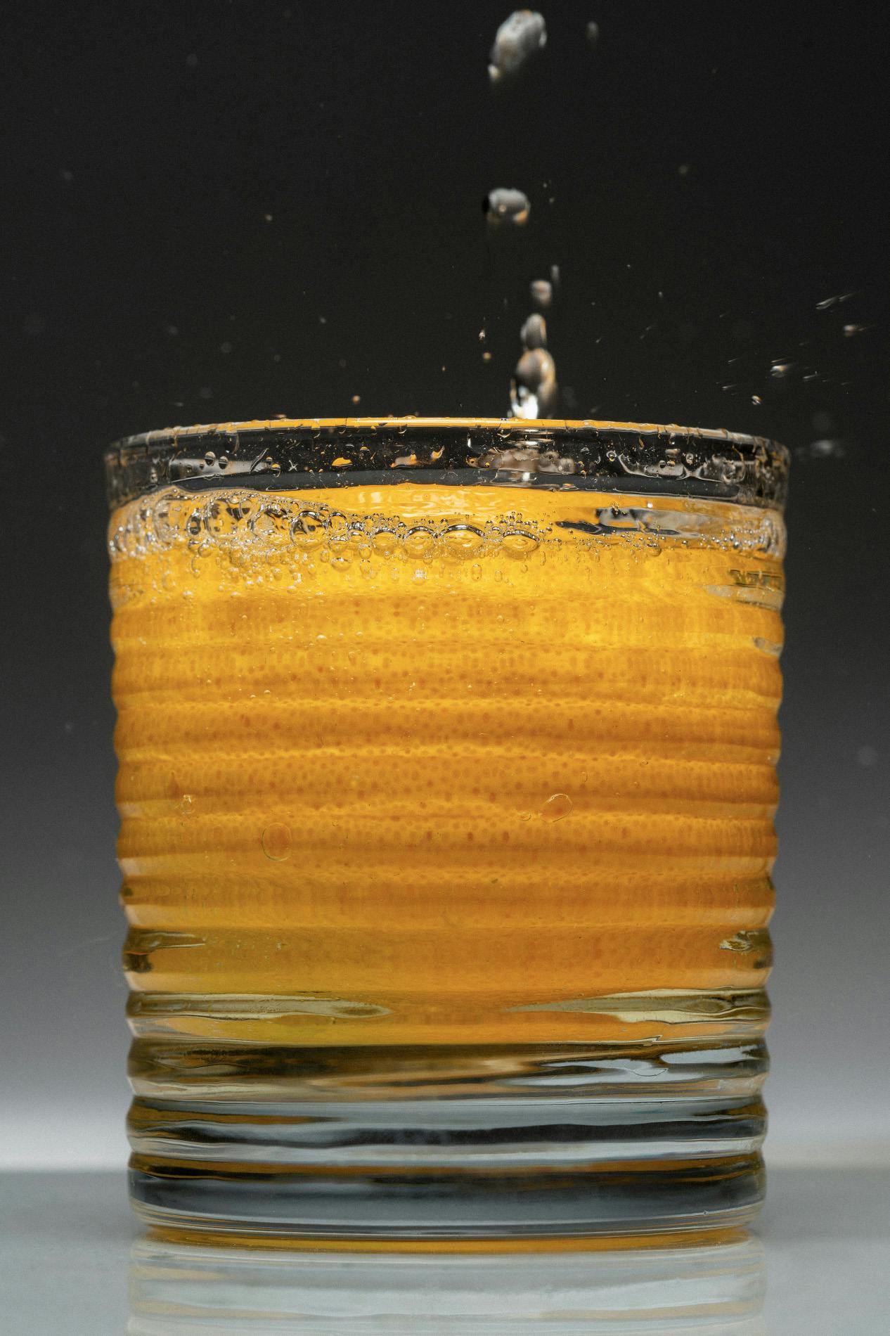 Cocktail glass with submerged orange and liquor falling on top