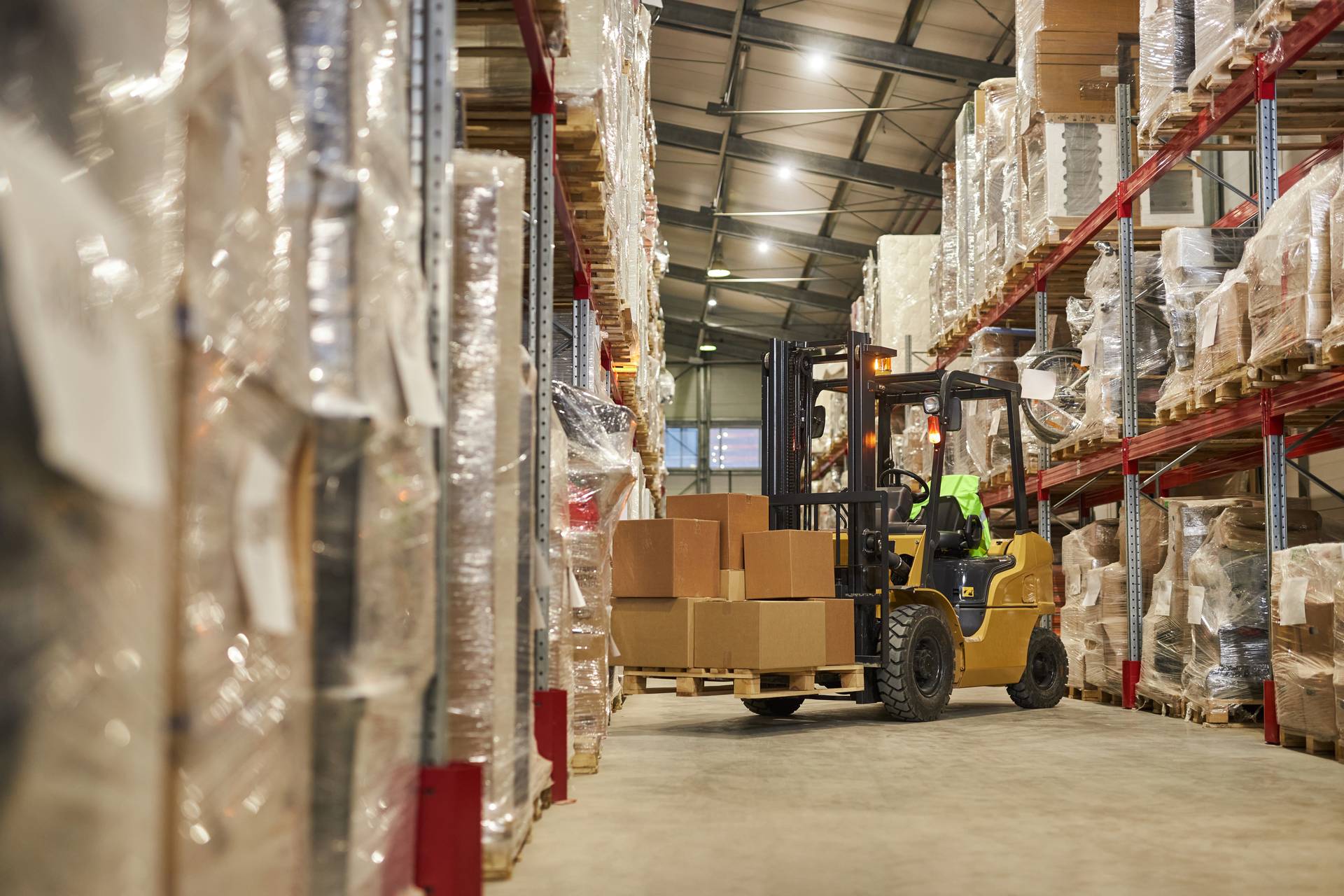 Materialfluss in der Produktion: Gabelstapler transportiert Kartons zwischen Palettenregalen im Lager