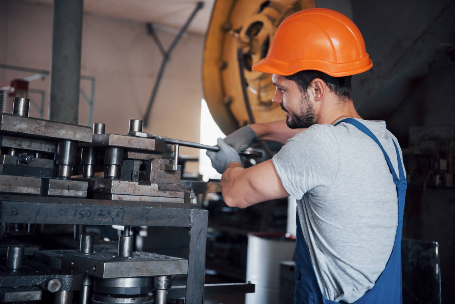 Monteur bei der mechanischen Montage: Werkzeugeinbau an einer Presse mit Schutzhelm und Handschuhen