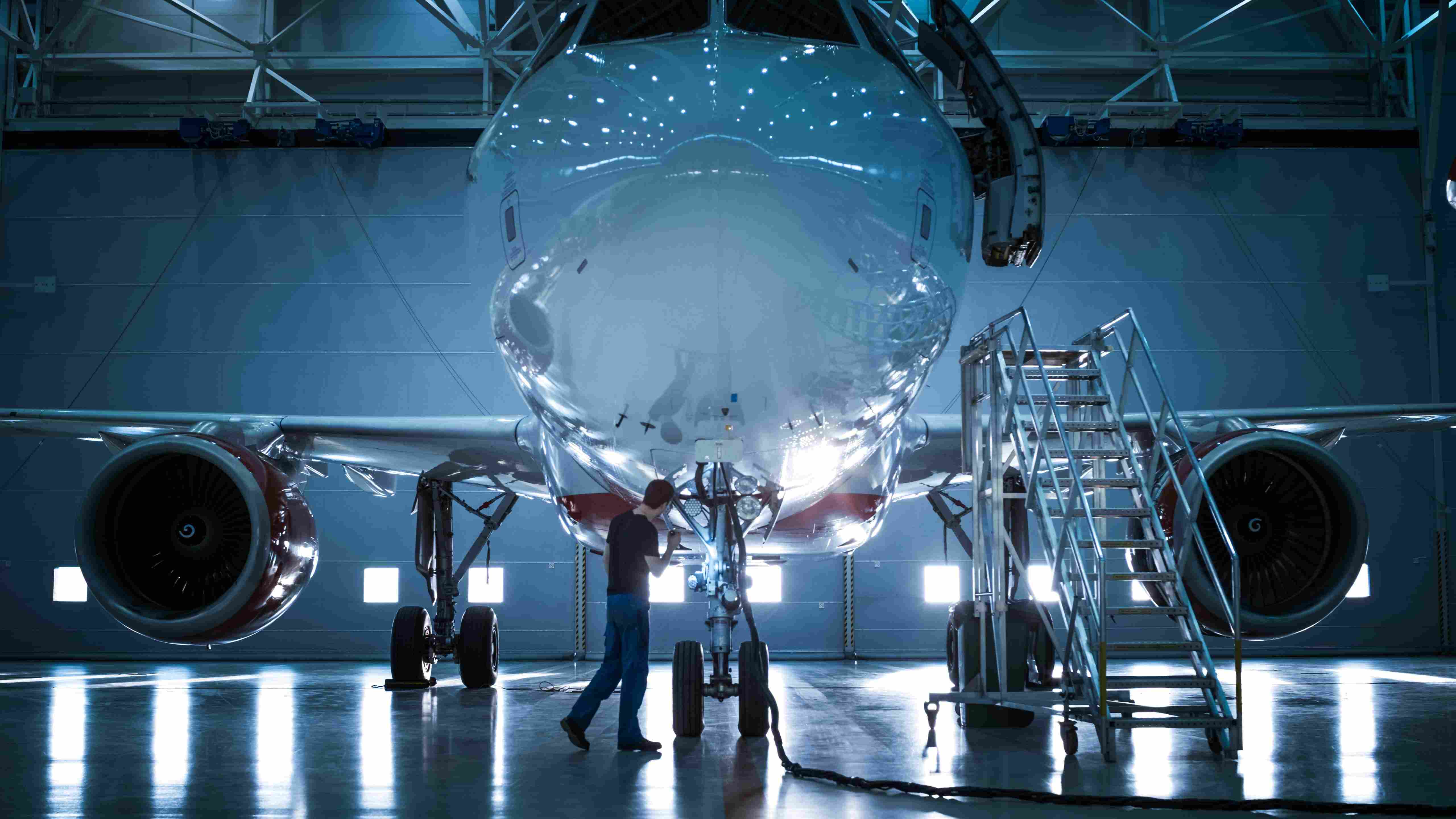 Ein Flugzeug welches in einer Halle steht und ein Mensch davor rum läuft und checks durchführt.