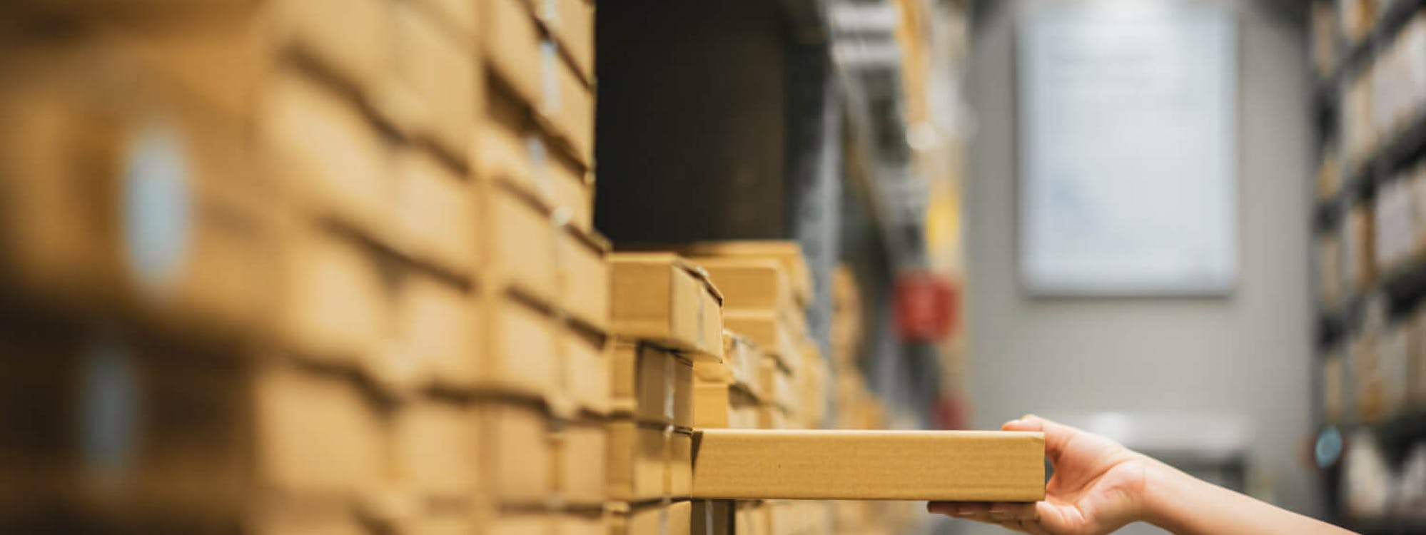 Hand greift in einem Lagerregal nach einem Paket – Symbolbild für effiziente Inbound-Logistik und strukturierte Warenannahmeprozesse.