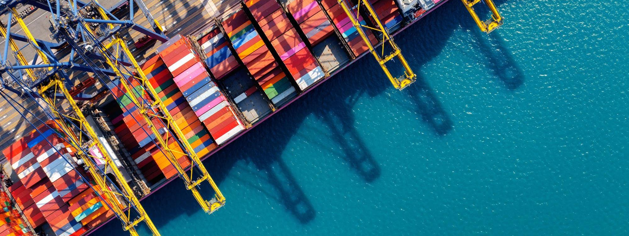 Luftaufnahme eines Containerhafens mit bunten Frachtcontainern und Kränen – Symbol für Zollabwicklung und internationale Logistikprozesse