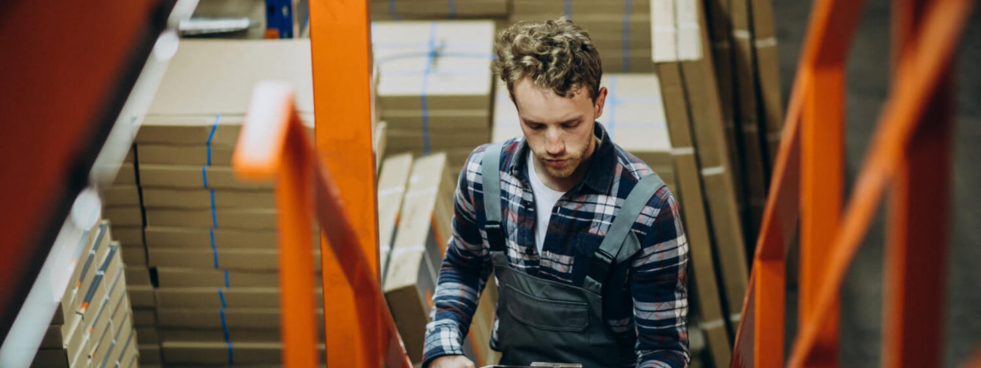 Mitarbeiter im Lager überprüft Bestände mit Tablet – Kontrolle und Berechnung des Meldebestands für eine effiziente Lagerverwaltung.