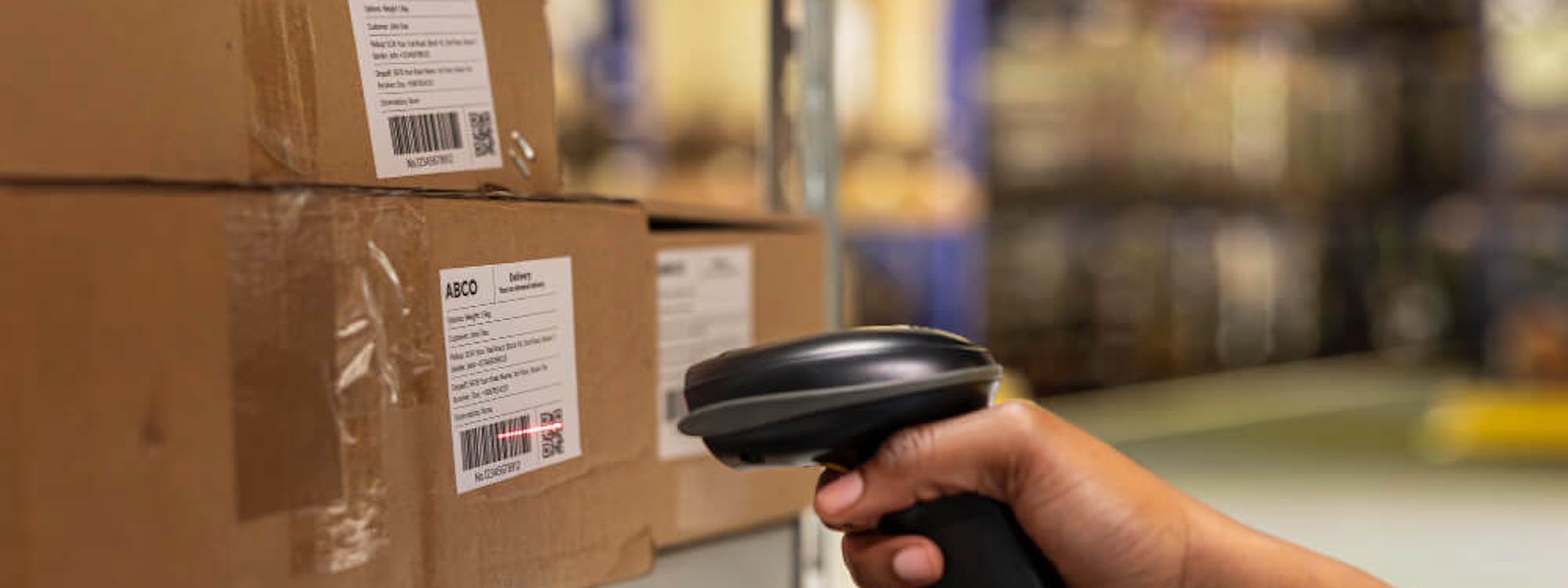 Mitarbeiter scannt Barcode auf Paket im Lager mit Handscanner – Pick-by-Scan als Methode der beleglosen Kommissionierung im Einsatz