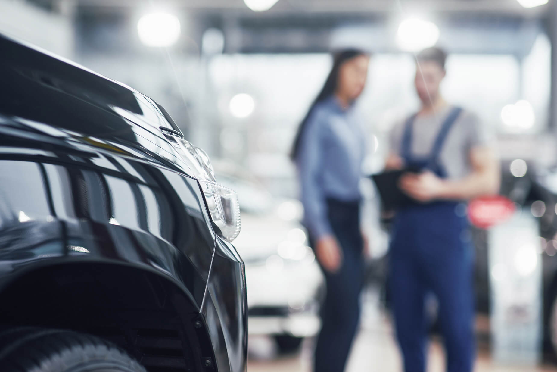 Zwei Arbeiter aus der Werkslogistik, die etwas vor einem neu hergestellten Auto planen