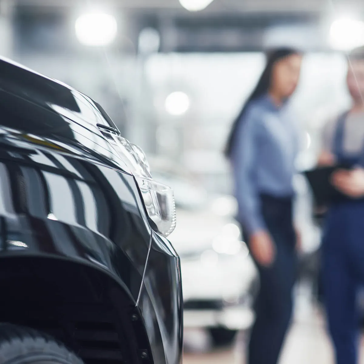 Zwei Arbeiter aus der Werkslogistik, die etwas vor einem neu hergestellten Auto planen