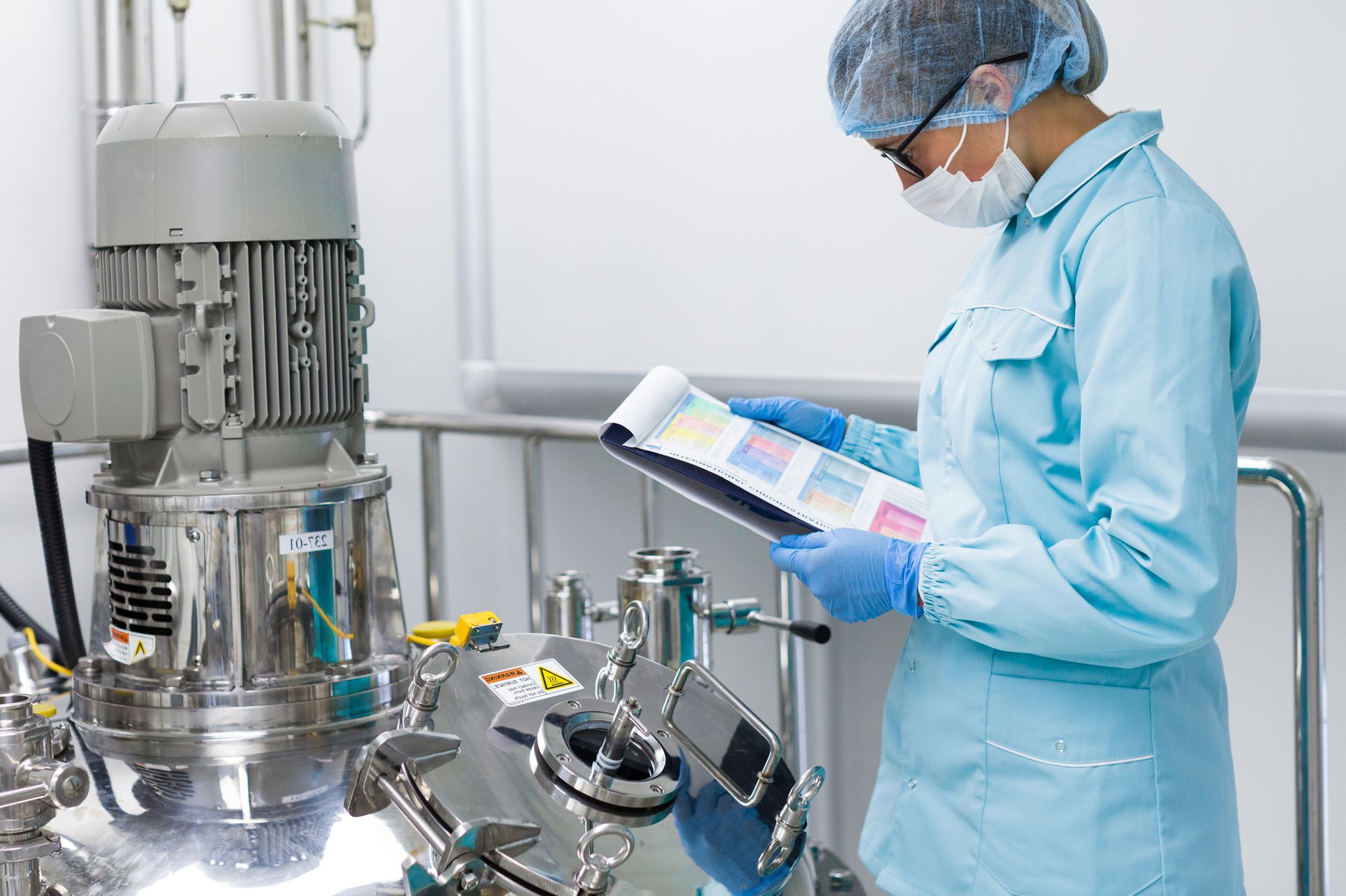Fachkraft mit Schutzkleidung kontrolliert Qualitätsdaten an Produktionsanlage in der Chemie- und Pharmaindustrie